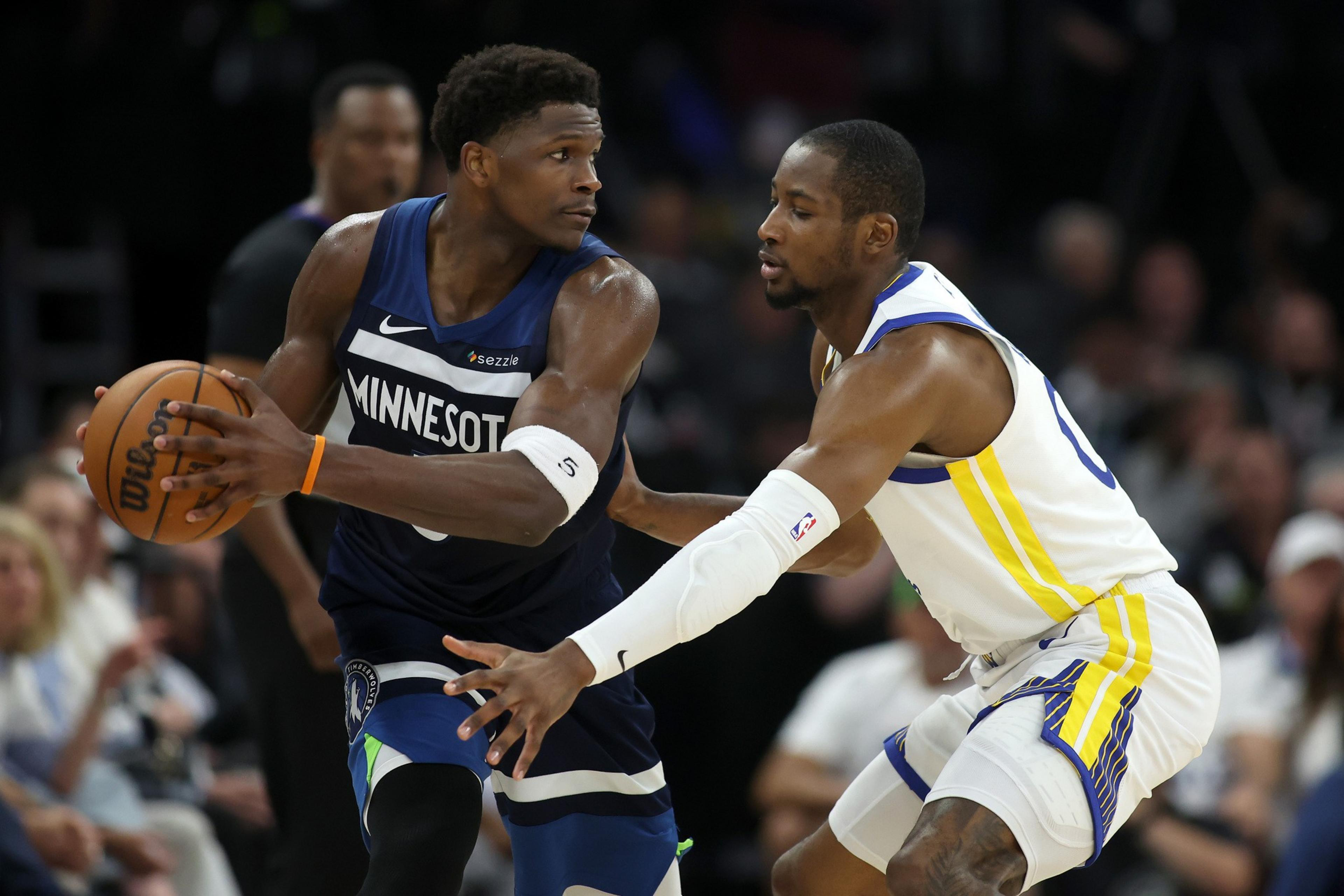 Two basketball players are in action; one in a blue &quot;Minnesota&quot; jersey holding the ball, closely guarded by a player in a white and yellow jersey.