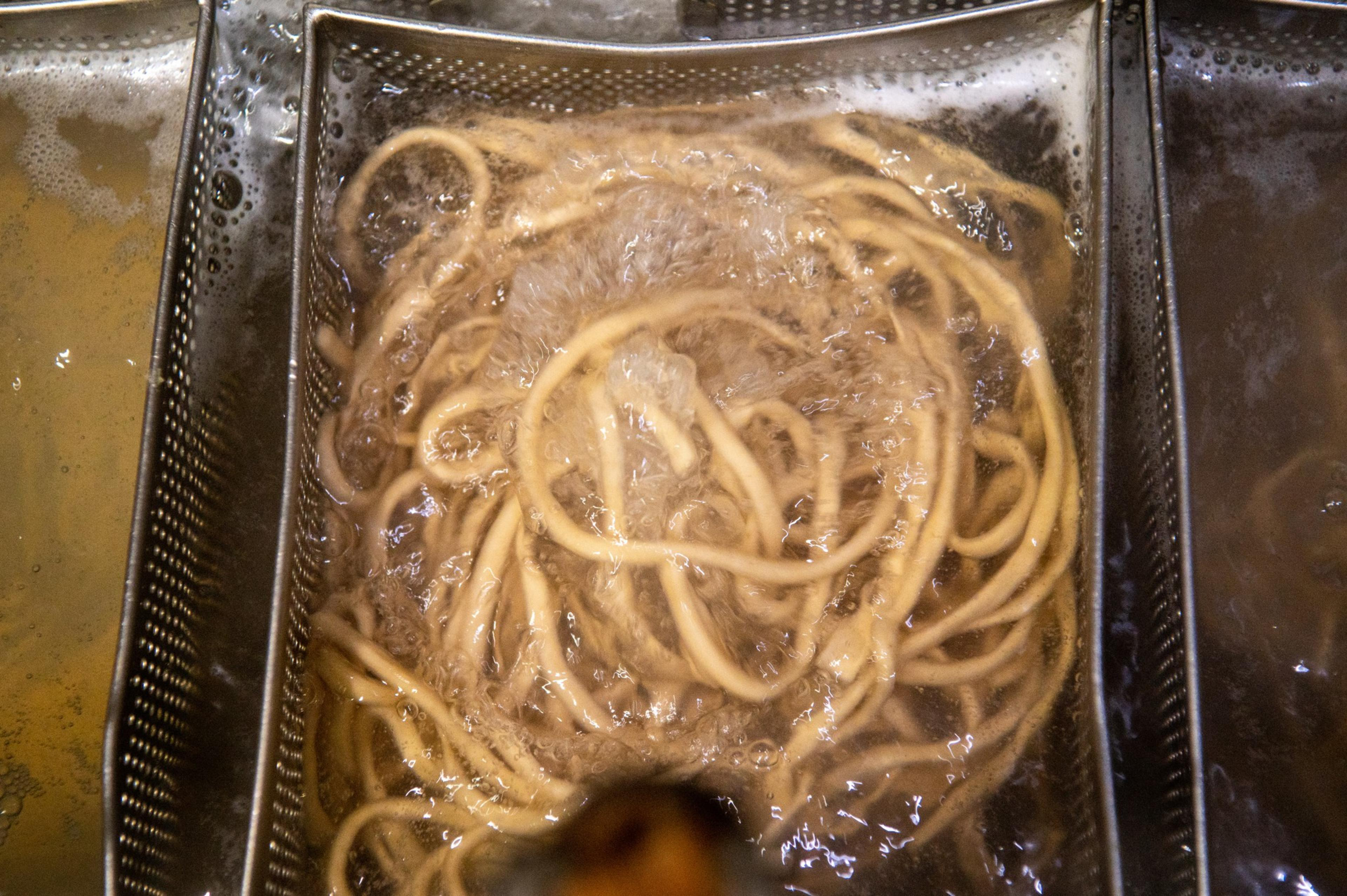 Noodles cook in a metal basket.
