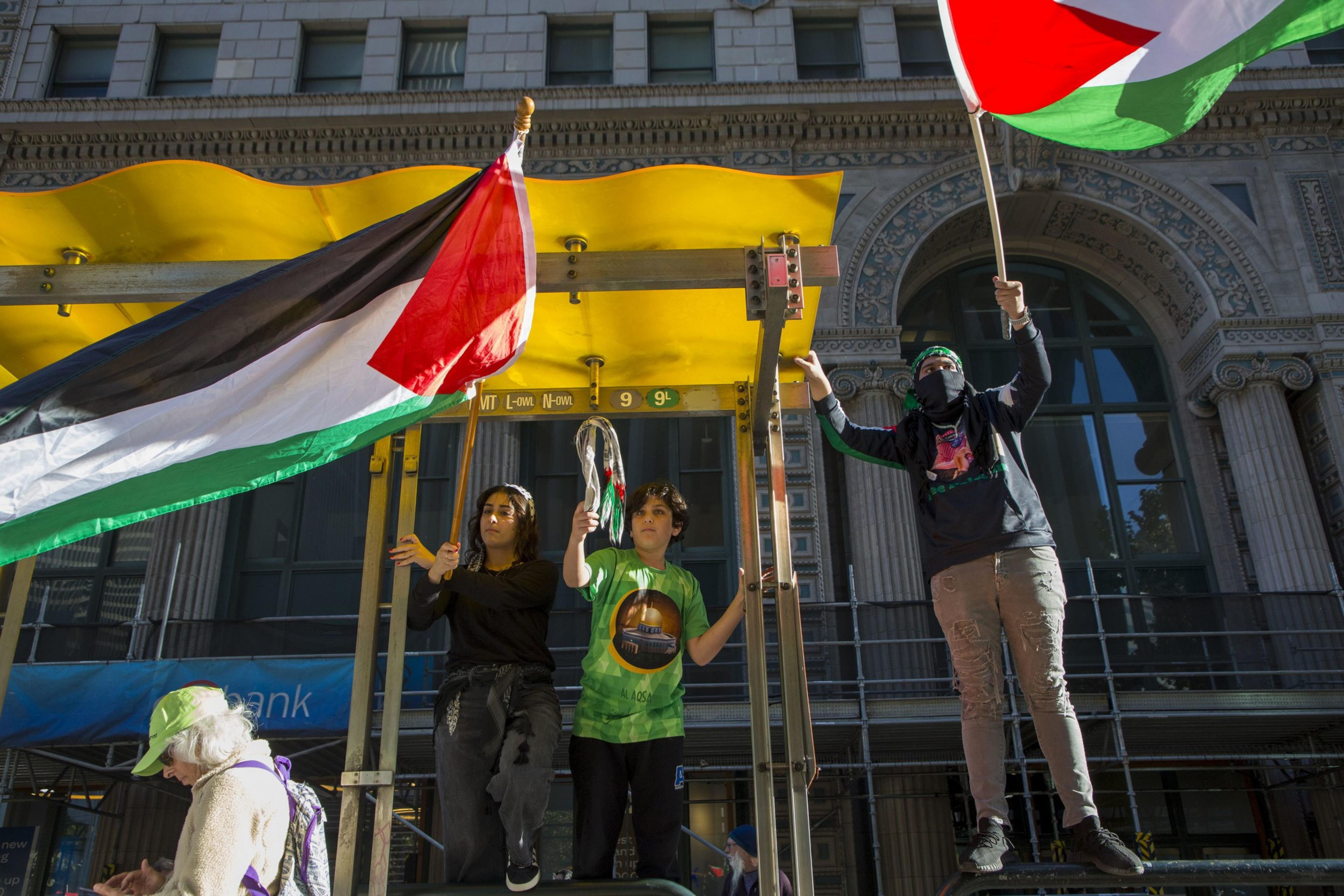 During the No 2 APEC march, three individuals stood atop a bus stop waving the Palestinian flag.