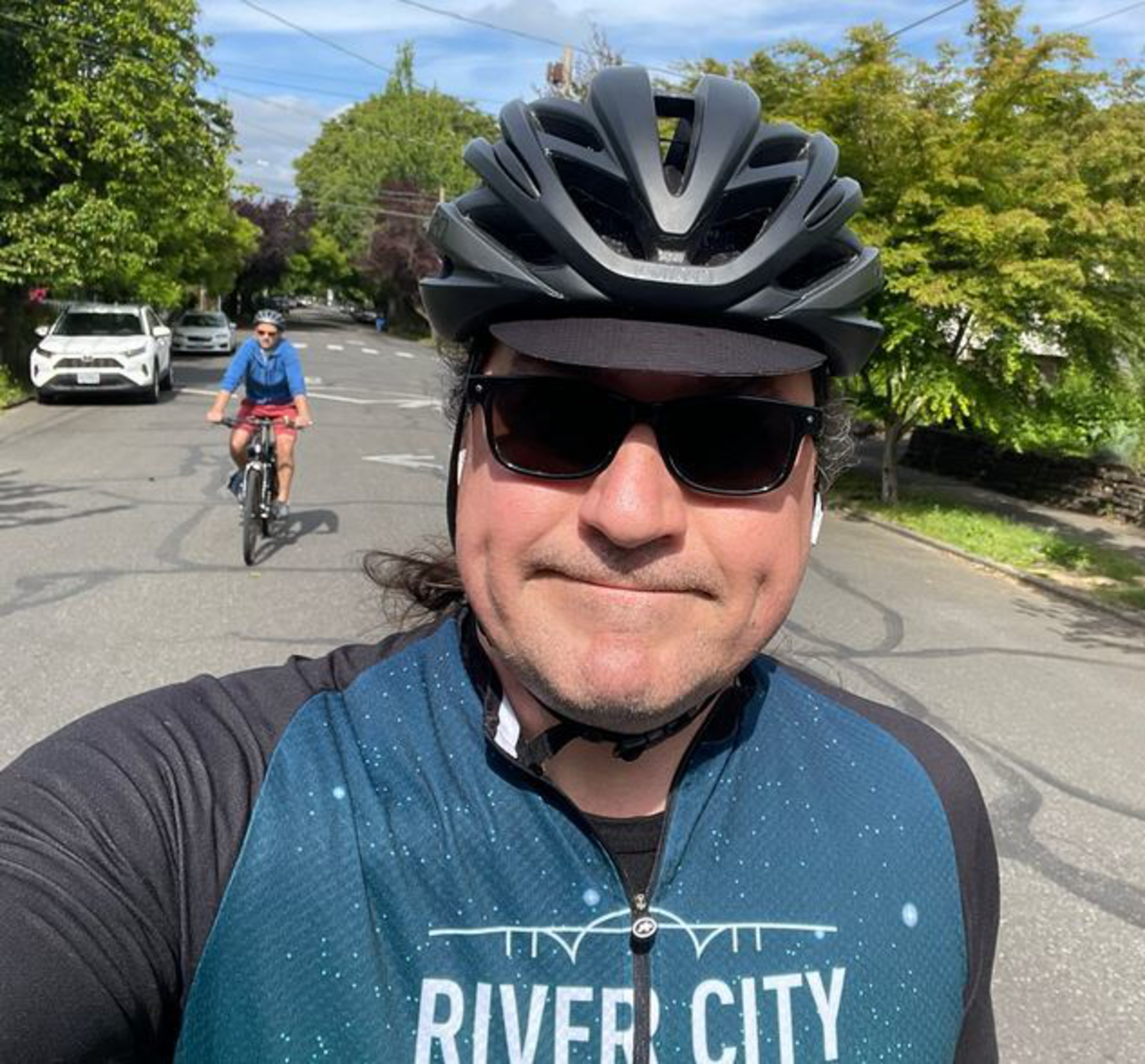 A man wearing a bike helmet and sunglasses stares into the camera.