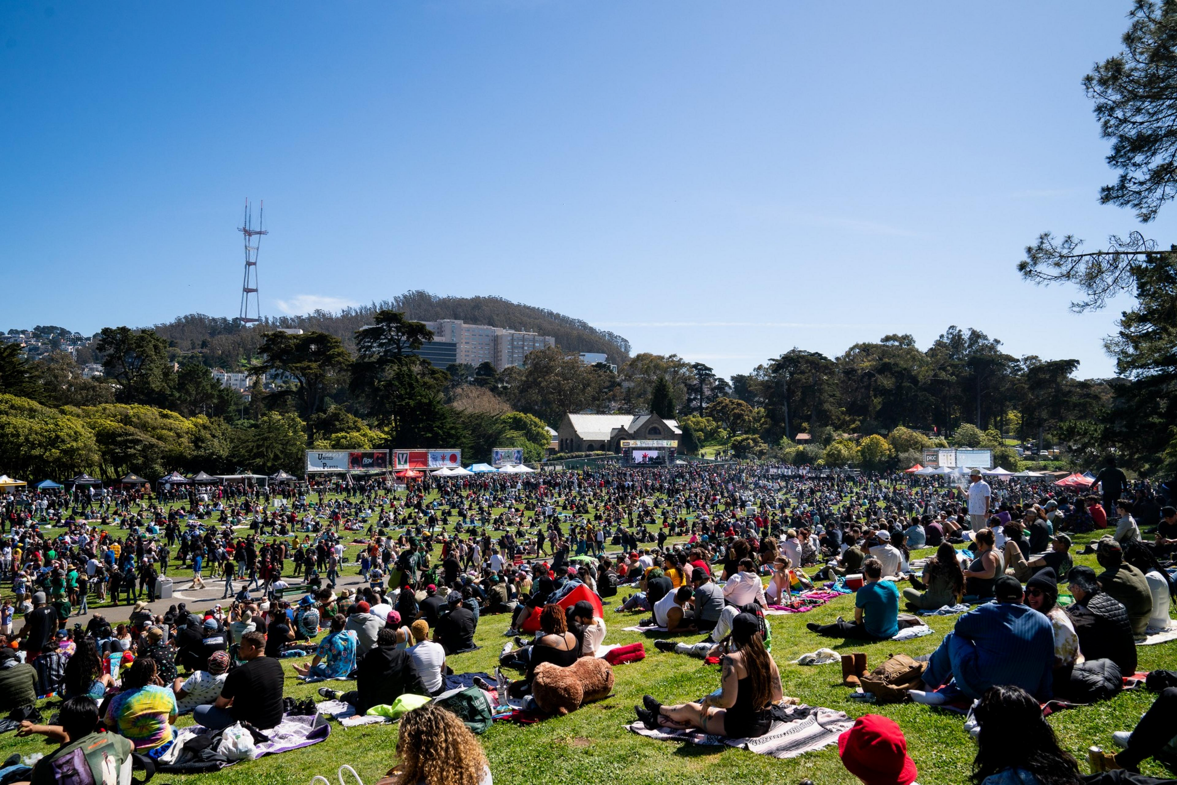 Thousands of people sit on grass, enjoying a sunny day at a large ...