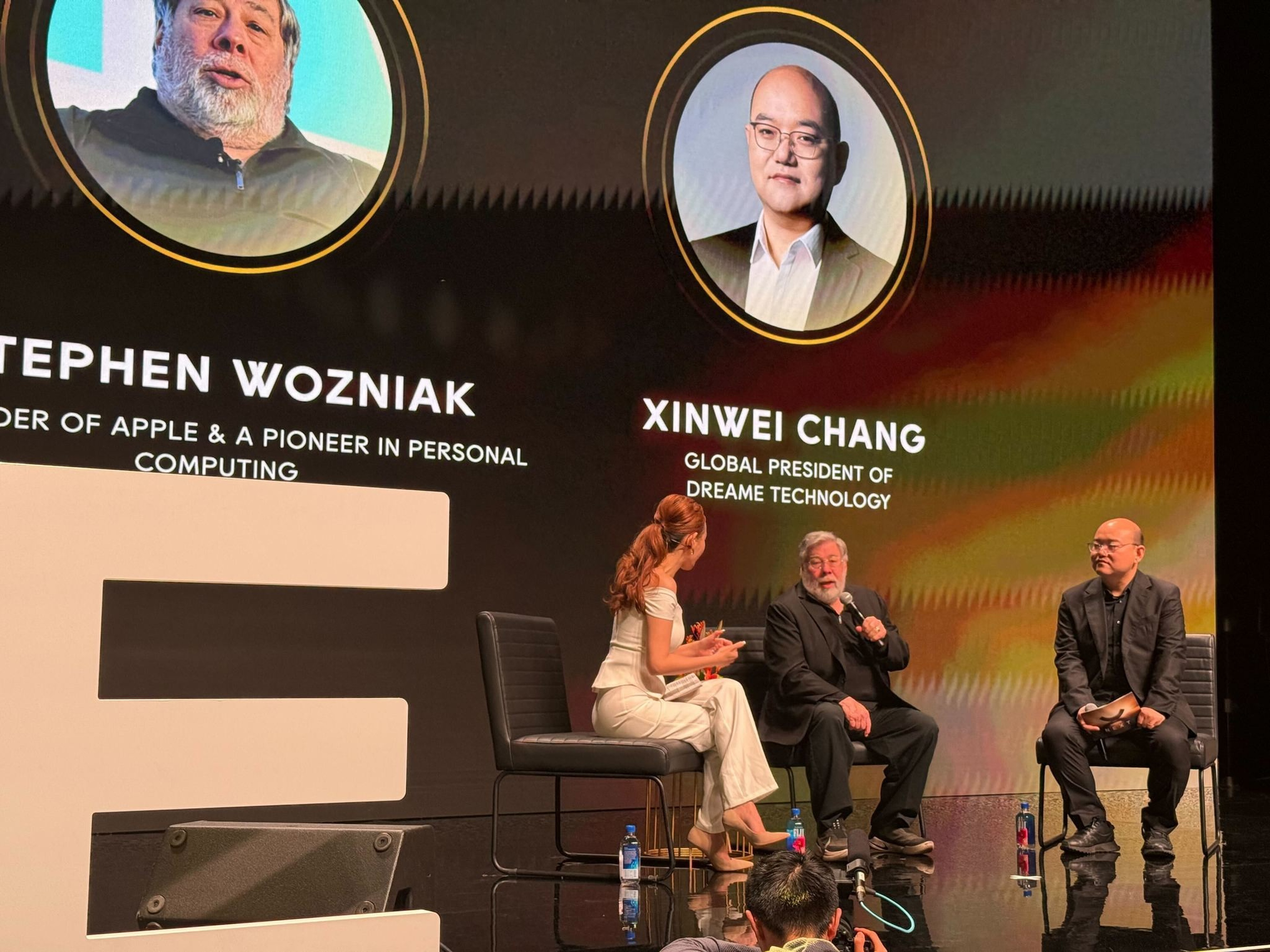 Three people sit on stage in discussion; behind them are large portraits and names of Stephen Wozniak, co-founder of Apple, and Xinwei Chang, global president of Dreame Technology.