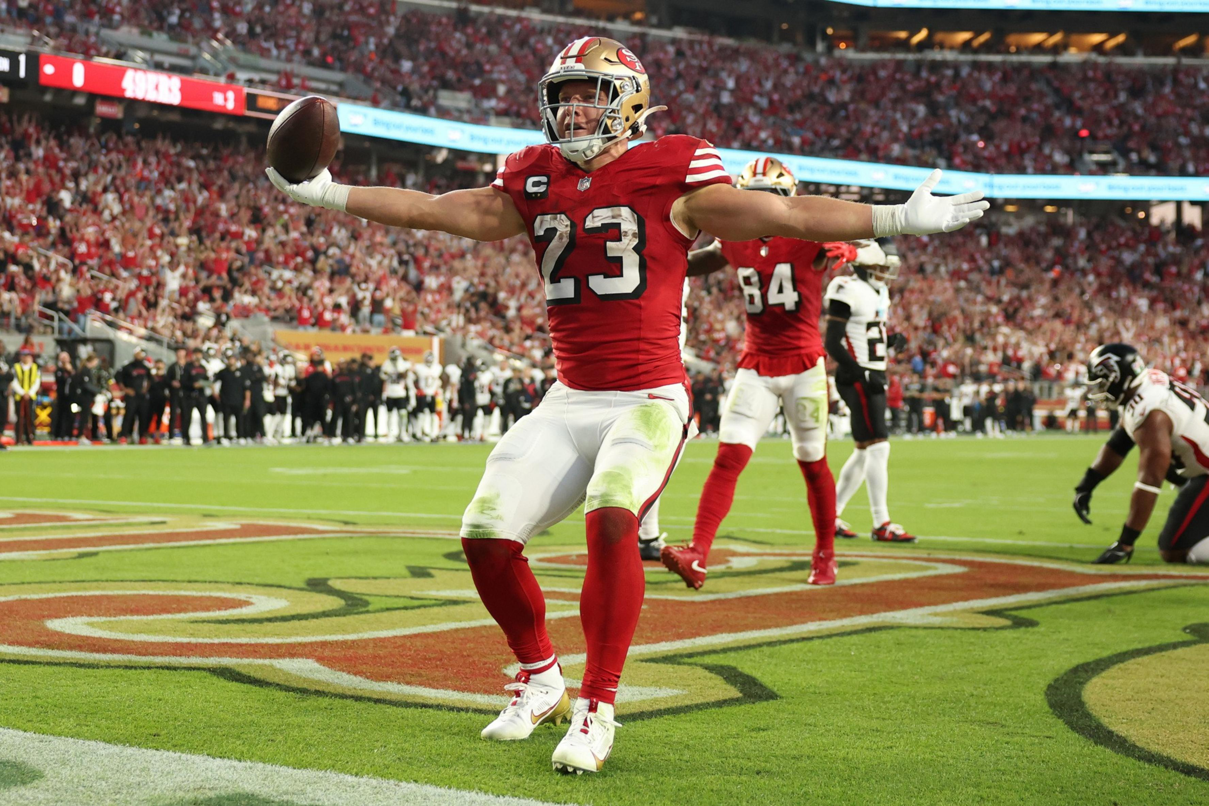 A football player in a red and white uniform, number 23, celebrates with arms outstretched in the end zone while holding the ball during a game.
