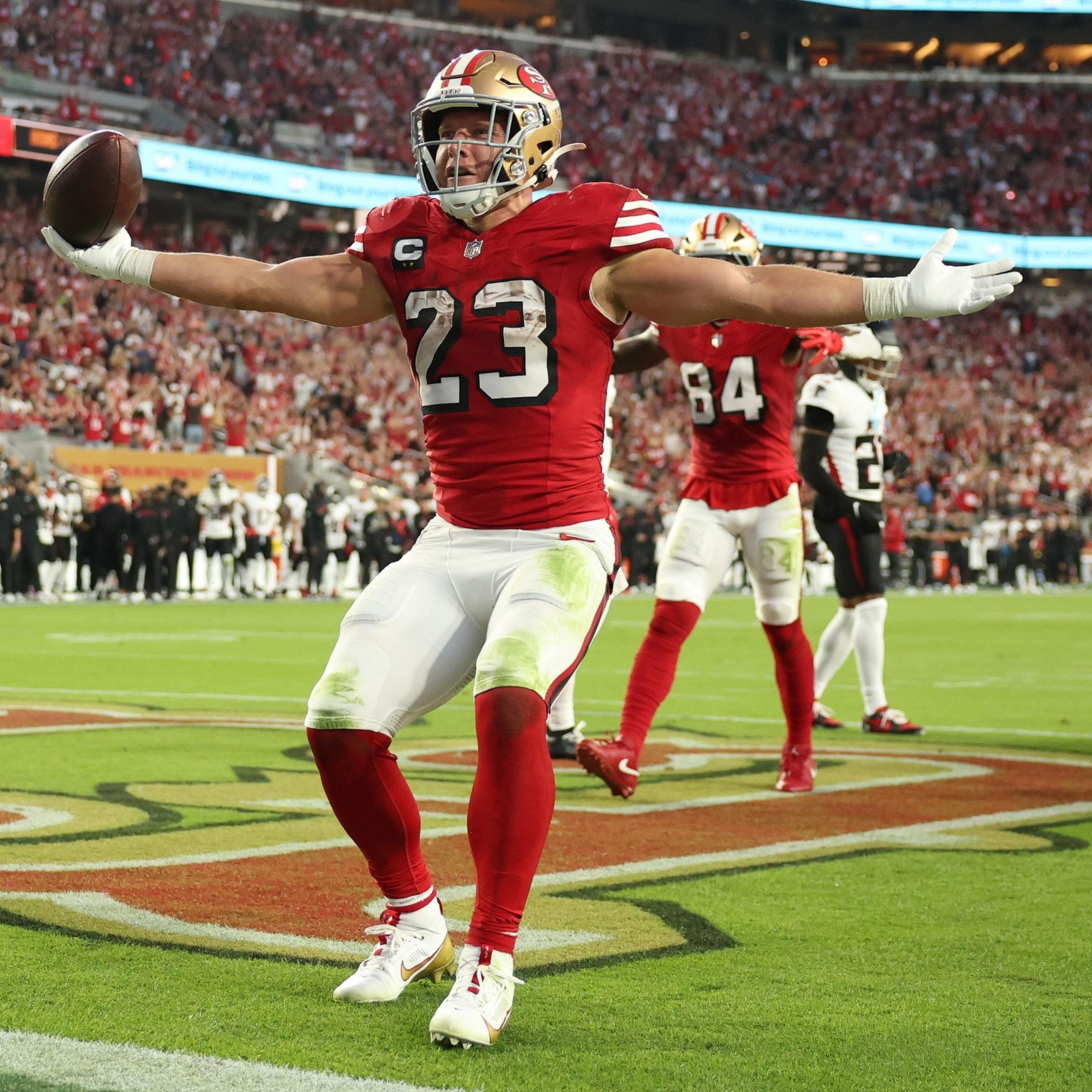 A football player in a red and white uniform, number 23, celebrates with arms outstretched in the end zone while holding the ball during a game.