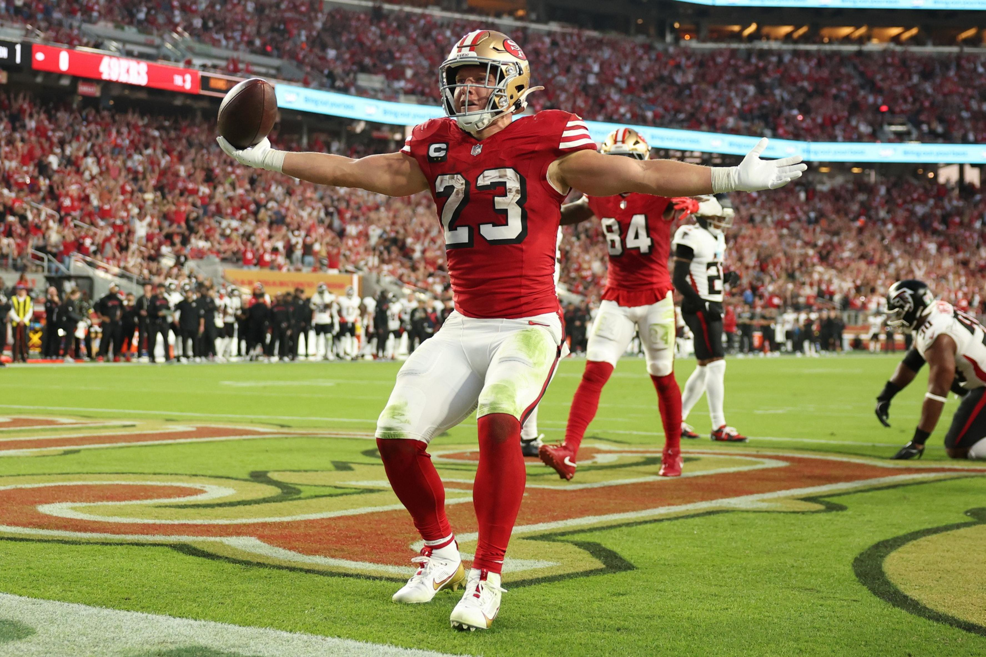 A football player in a red and white uniform, number 23, celebrates with arms outstretched in the end zone while holding the ball during a game.