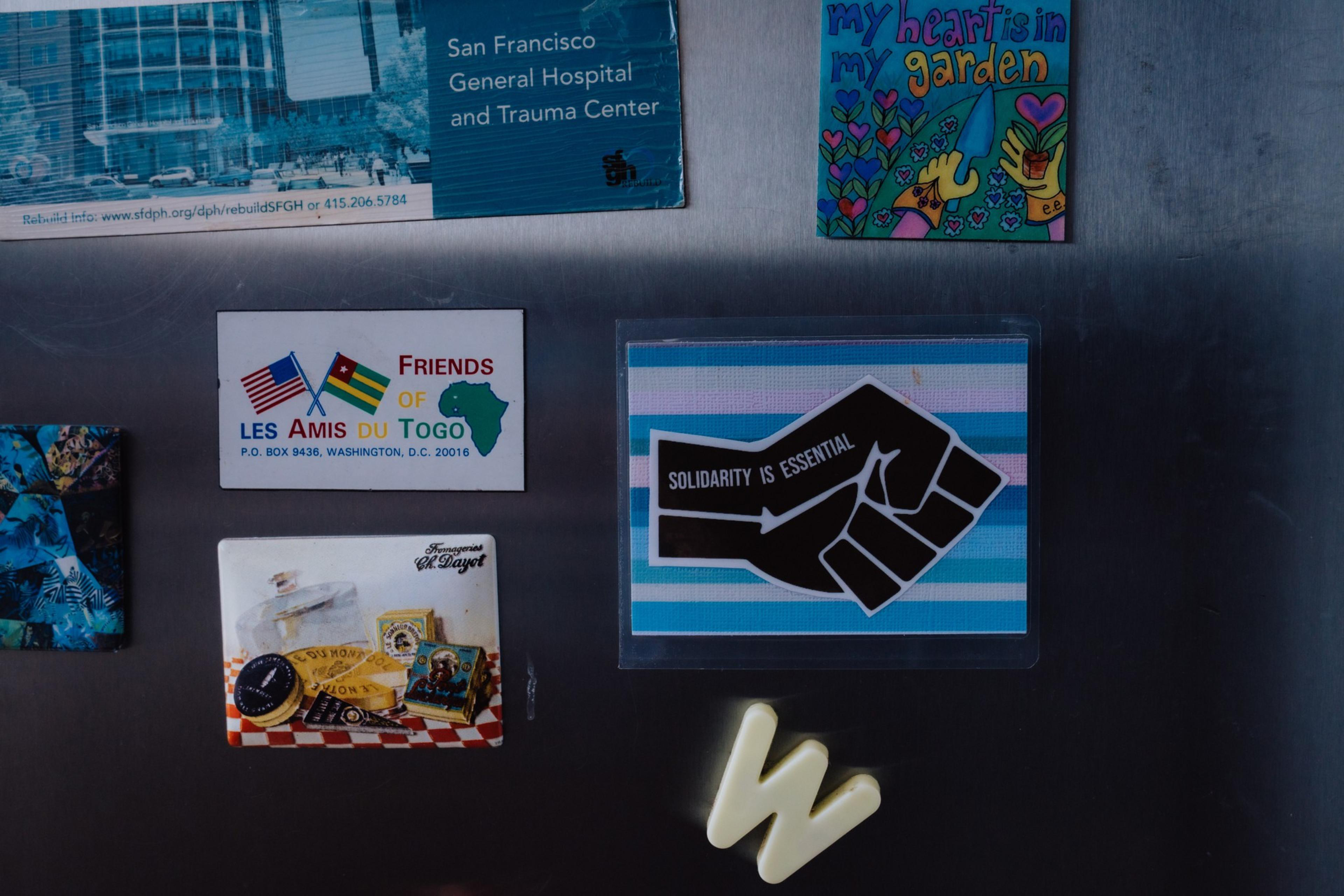 The image shows colorful magnets on a metallic surface, including hospital info, a &quot;Friends of Togo&quot; logo, a &quot;Solidarity is Essential&quot; fist, and the letter &quot;W&quot;.