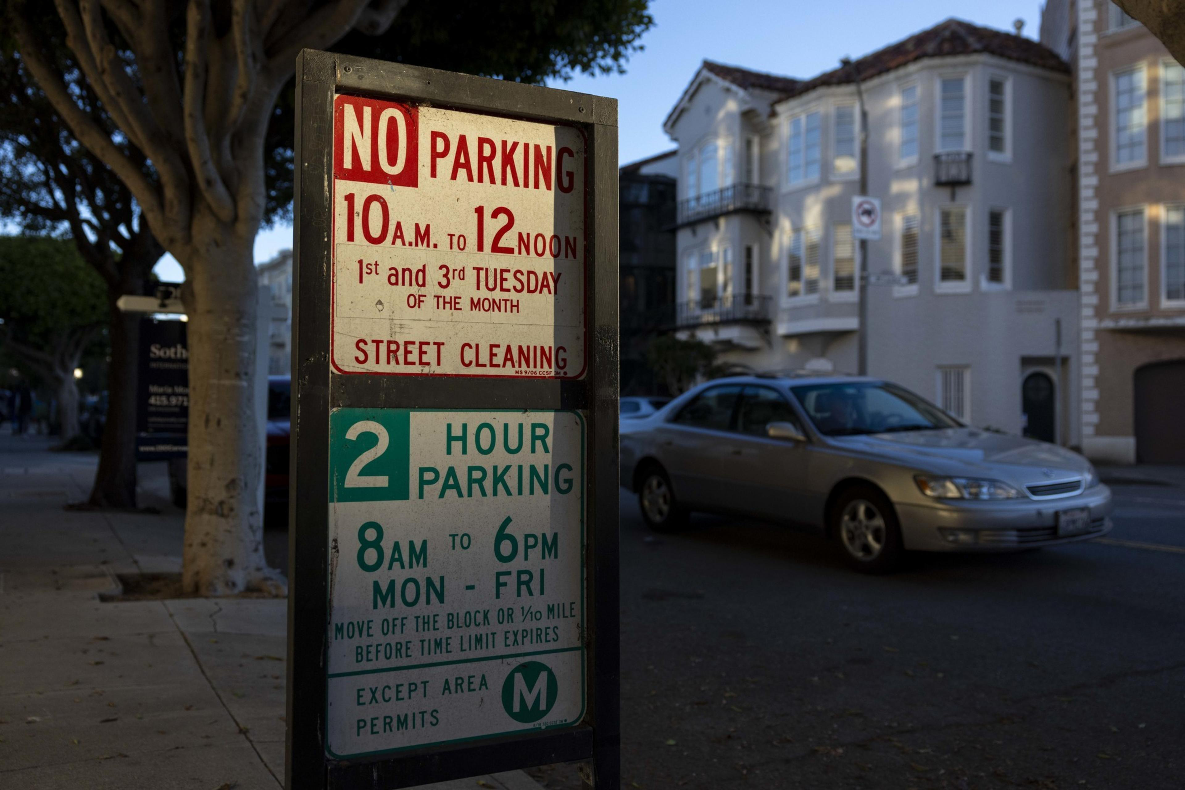 A parking sign states no parking from 10 a.m. to 12 noon on the 1st and 3rd Tuesday for street cleaning, and allows 2-hour parking from 8 a.m. to 6 p.m. on weekdays.