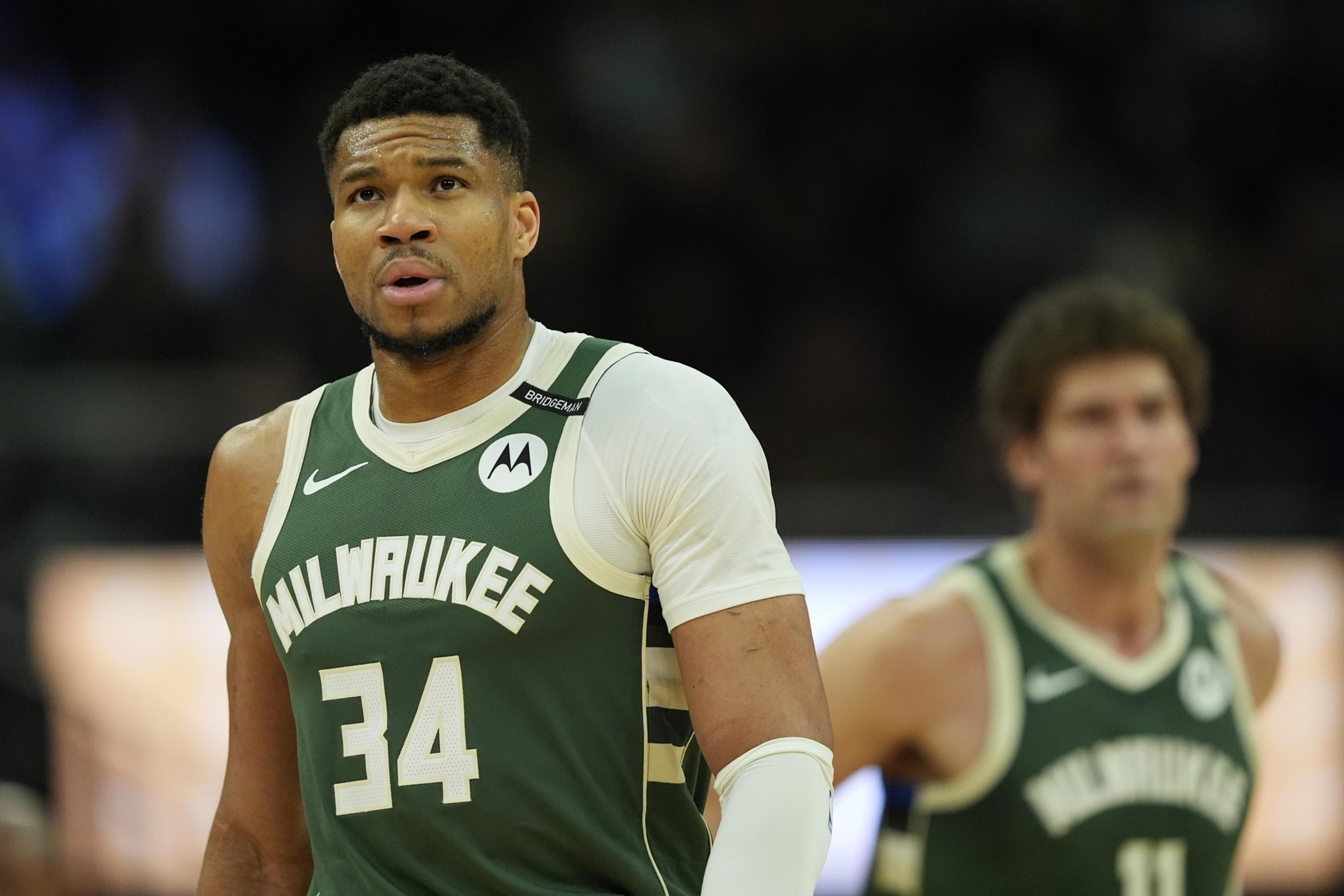 A basketball player in a green Milwaukee jersey with number 34 looks focused, while another player in the background is slightly out of focus.