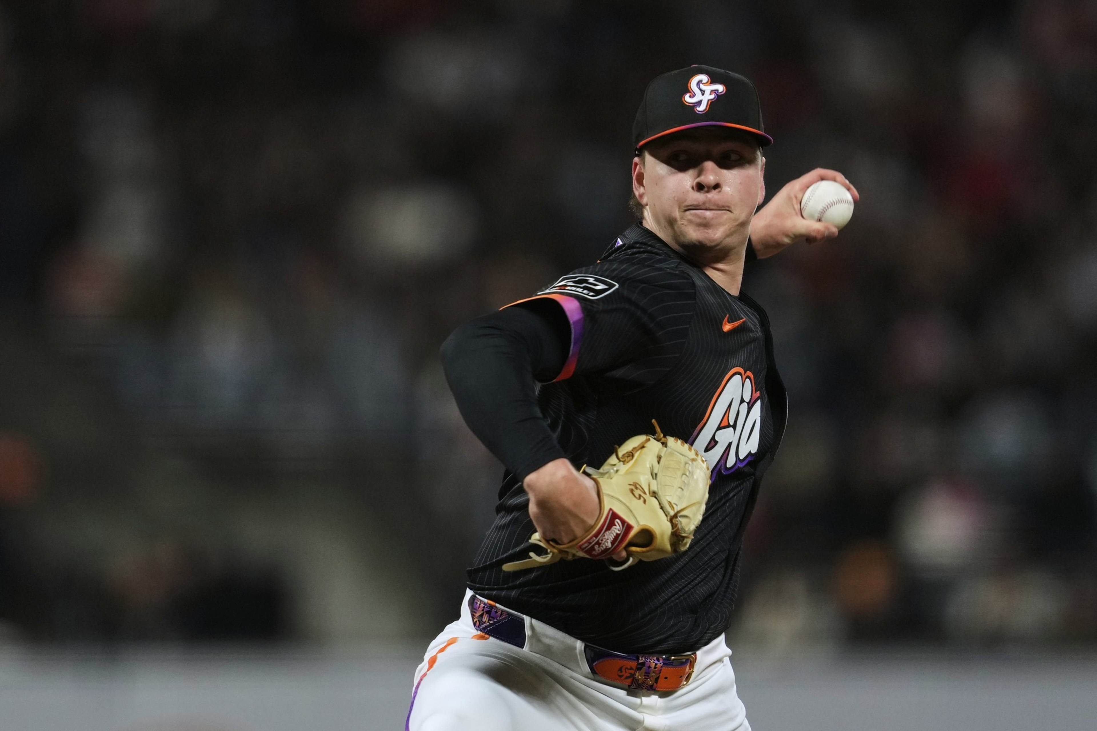 A baseball pitcher in a black uniform is mid-throw on the mound, wearing a cap with &quot;SF&quot; and holding a ball in his right hand and a glove on the left.