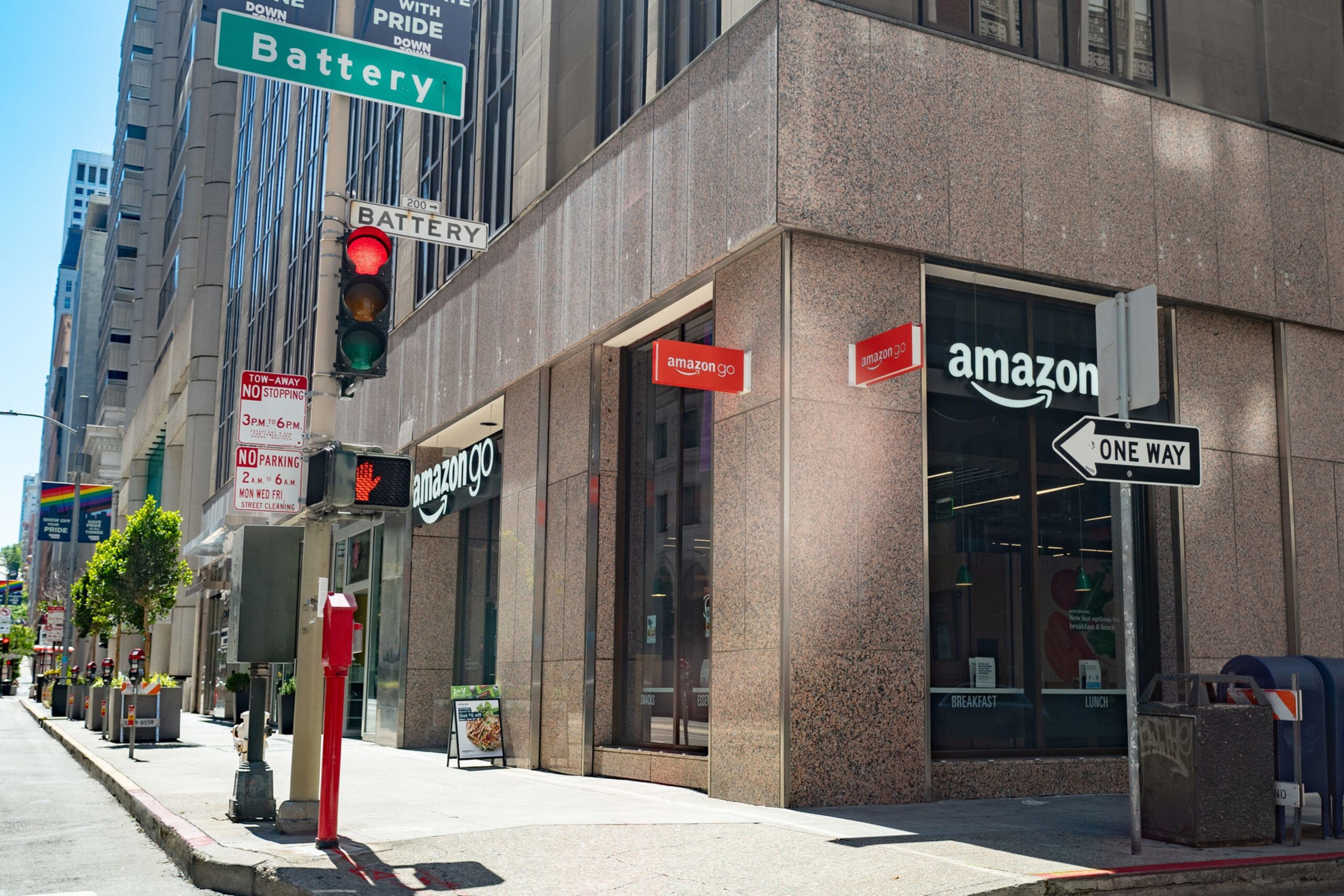 Corner storefront of an Amazon Go store on Battery Street with traffic lights, a one-way sign, and no parking/no stopping signs nearby.