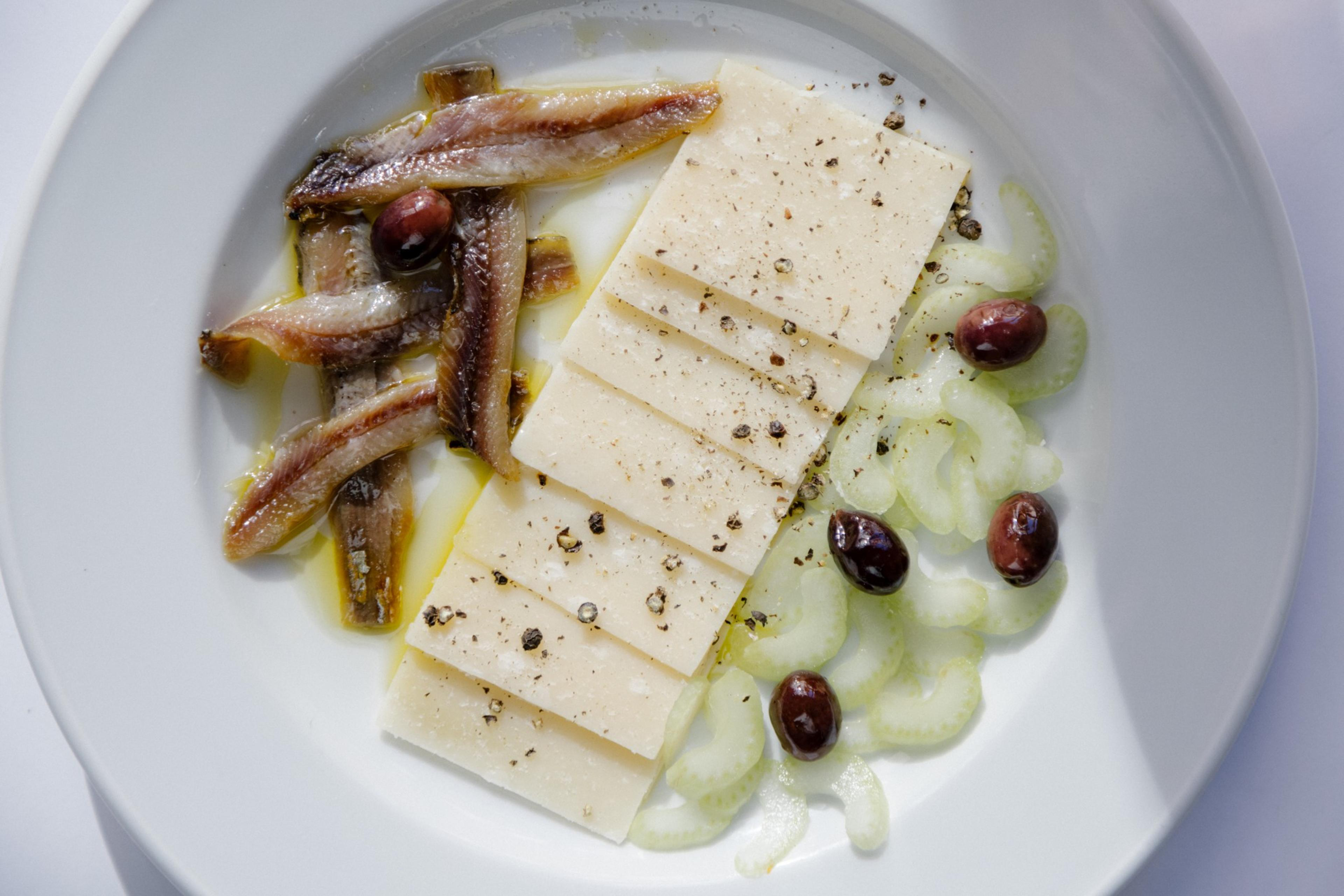 An over head view of a plate of house-cured anchovies with celery, Parmigiano-Reggiano and coquillo olives at Zuni Café.