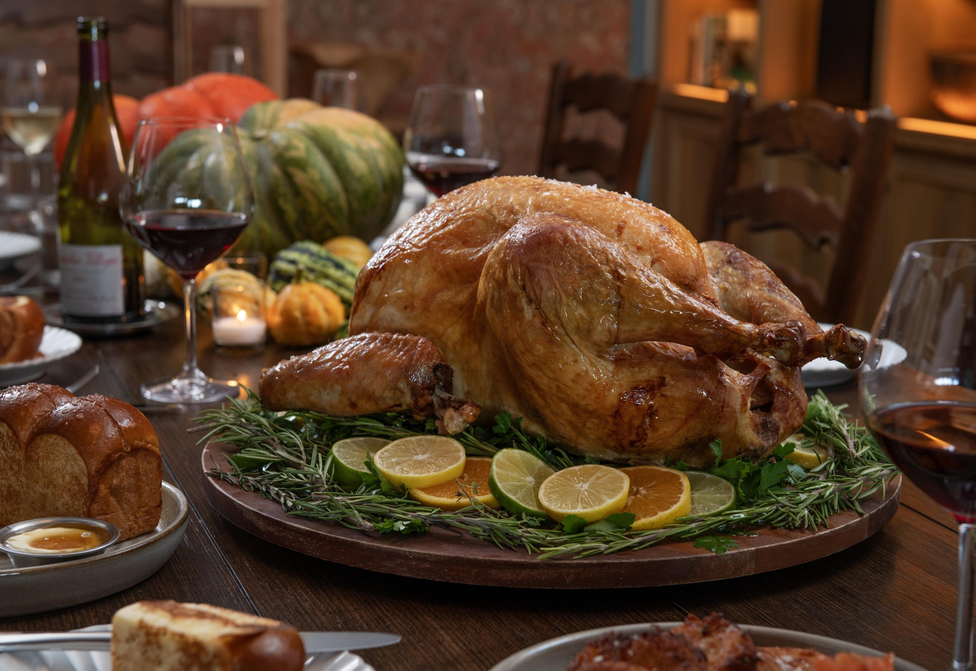 A picture of a whole cooked turkey on a dinner table full of dishes, including bread and wine.