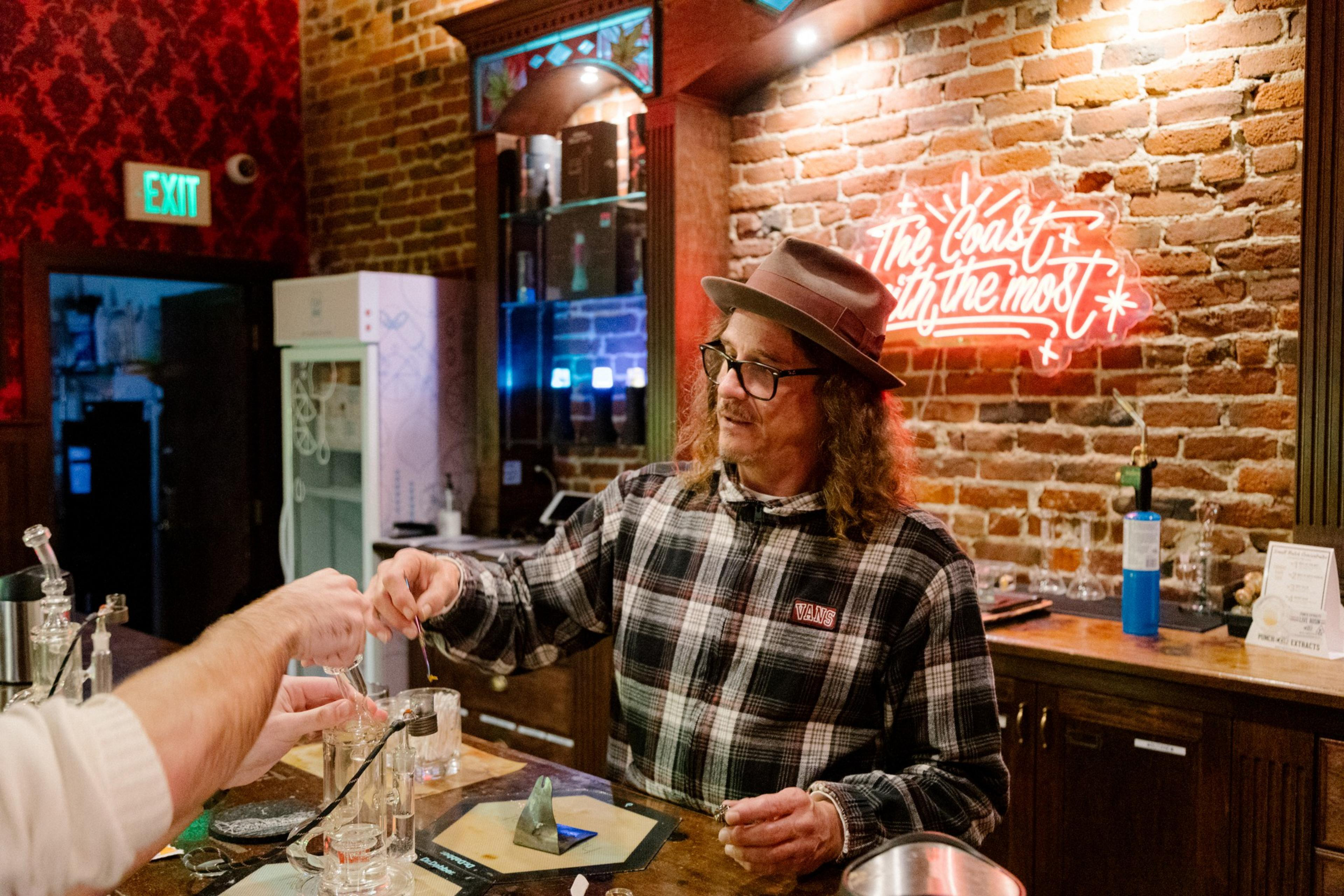 A man wearing a fedora hat stands behind a counter serving a customer.