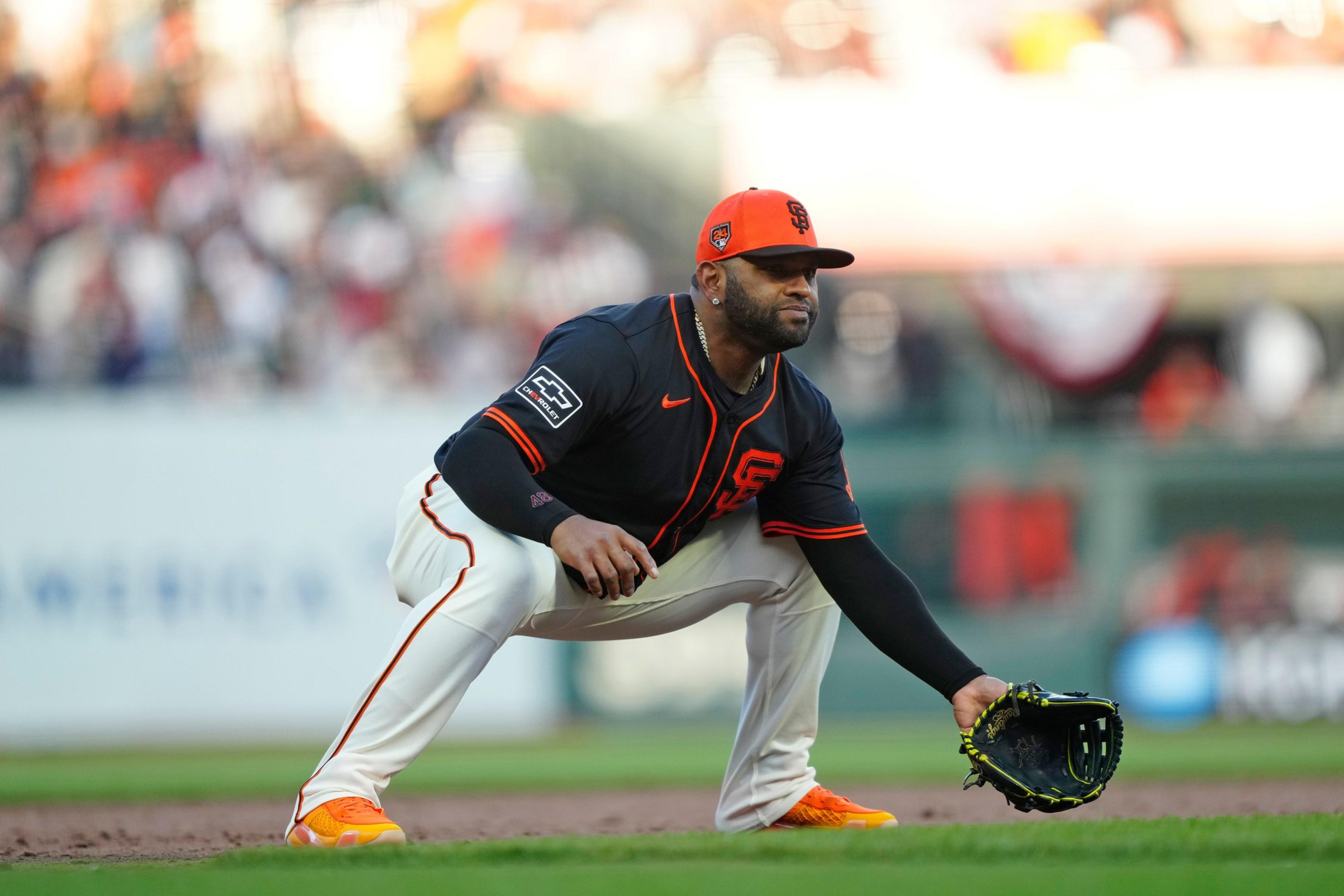 A baseball player in a black and orange San Francisco Giants uniform crouches in a ready fielding position on the infield dirt.