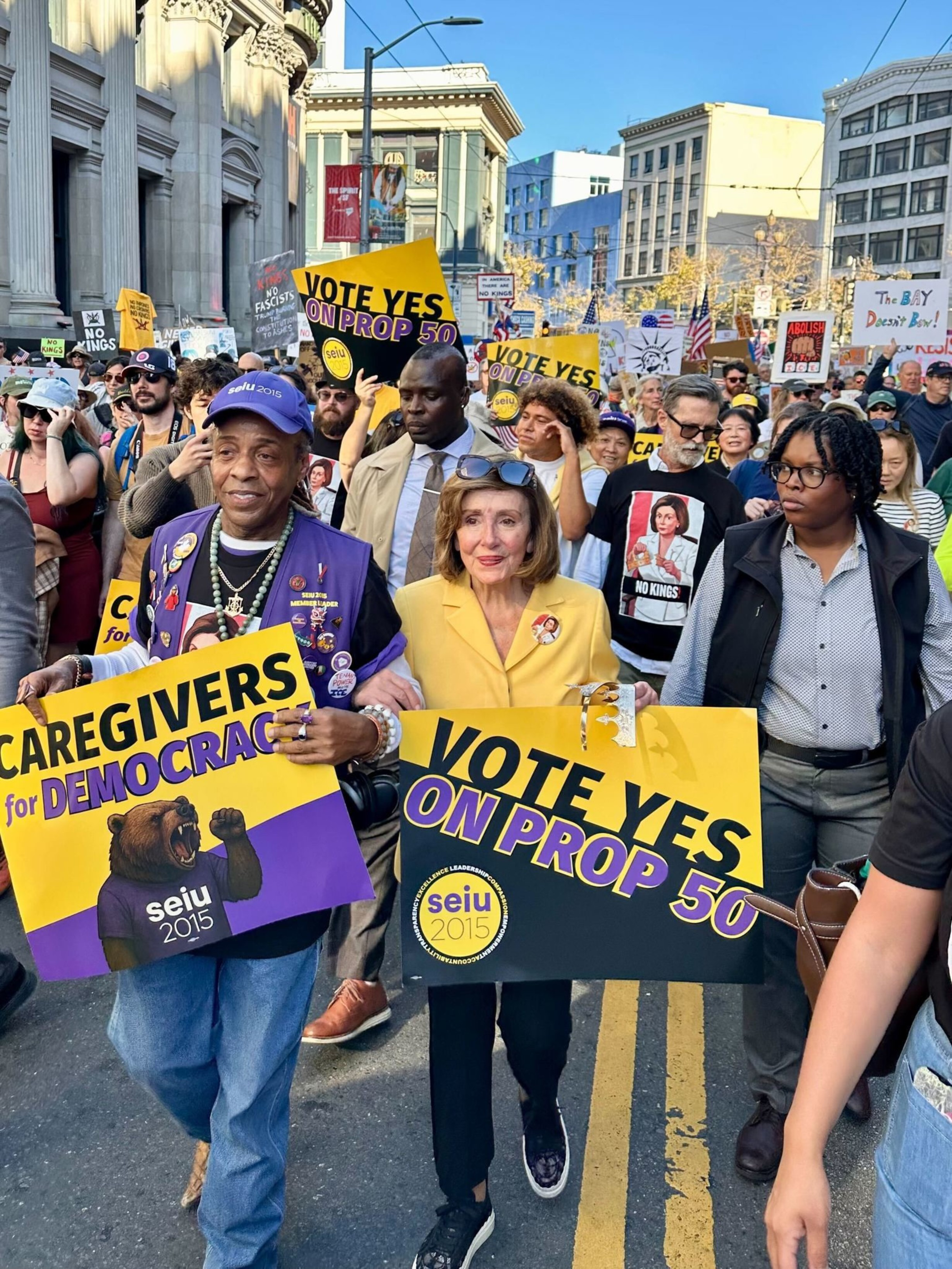 People march in a street protest holding signs that read “Vote Yes on Prop 50" and ”Caregivers for Democracy.”