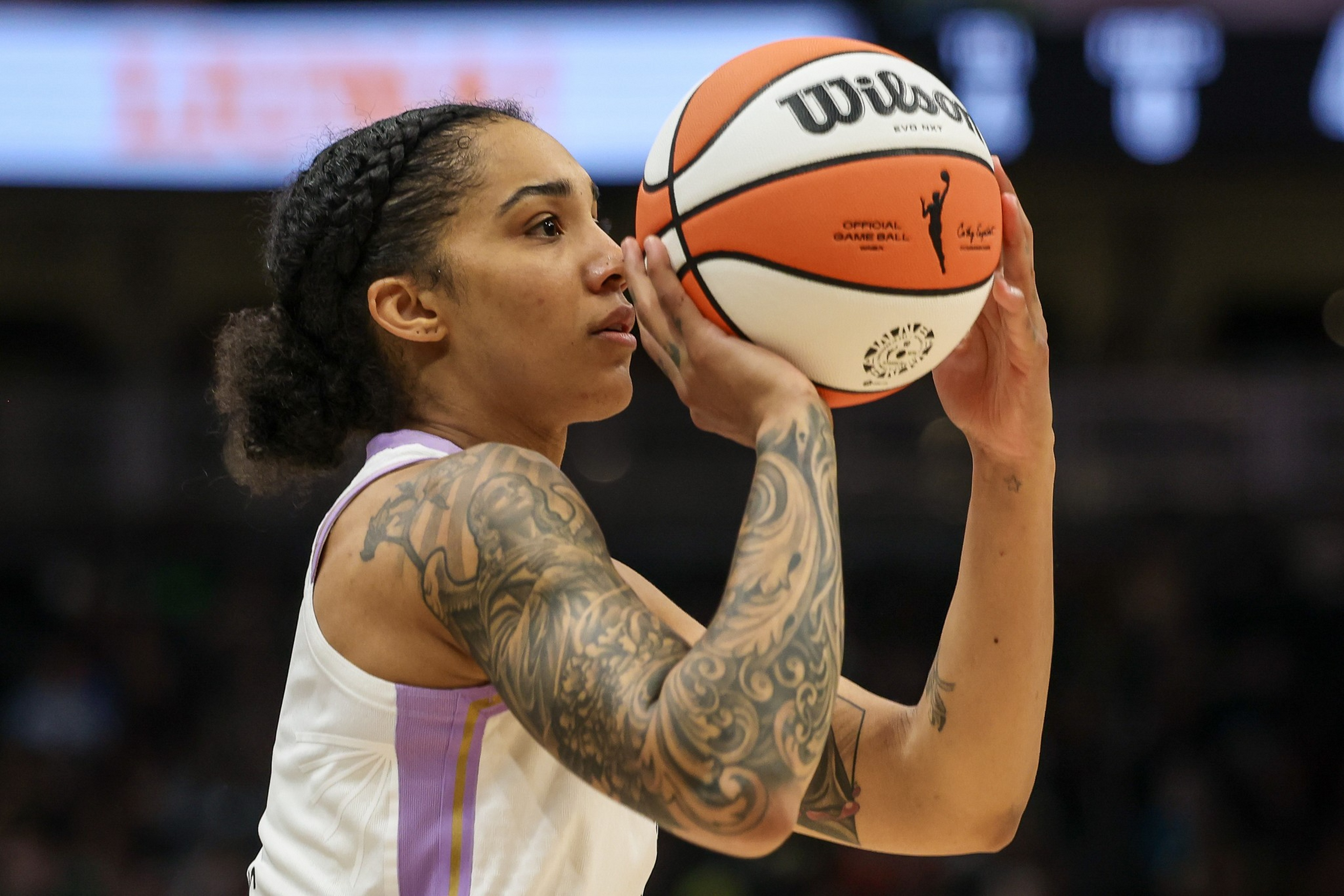 A female basketball player with braided hair and an arm tattoo focuses as she prepares to shoot a basketball during a game.