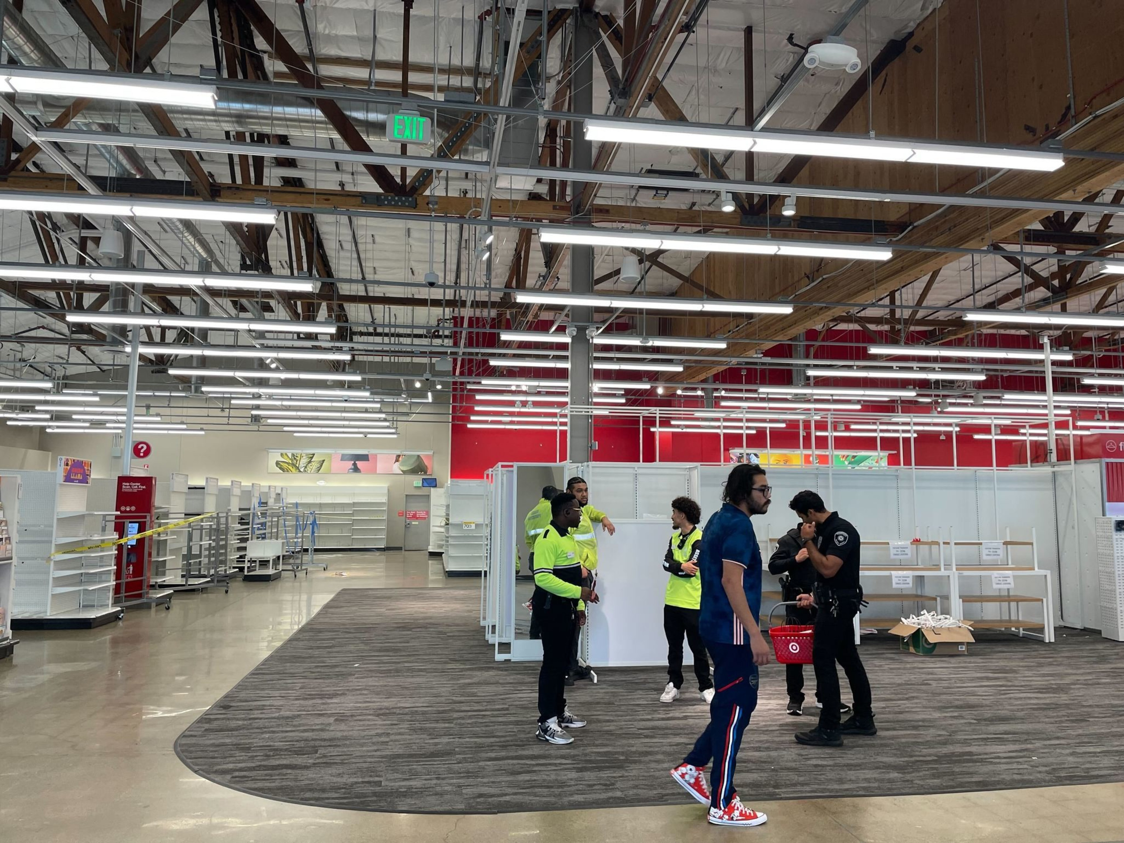Workers in casual clothes, including some wearing green vests, stand in an emptied out store under rows of fluorescent lights.