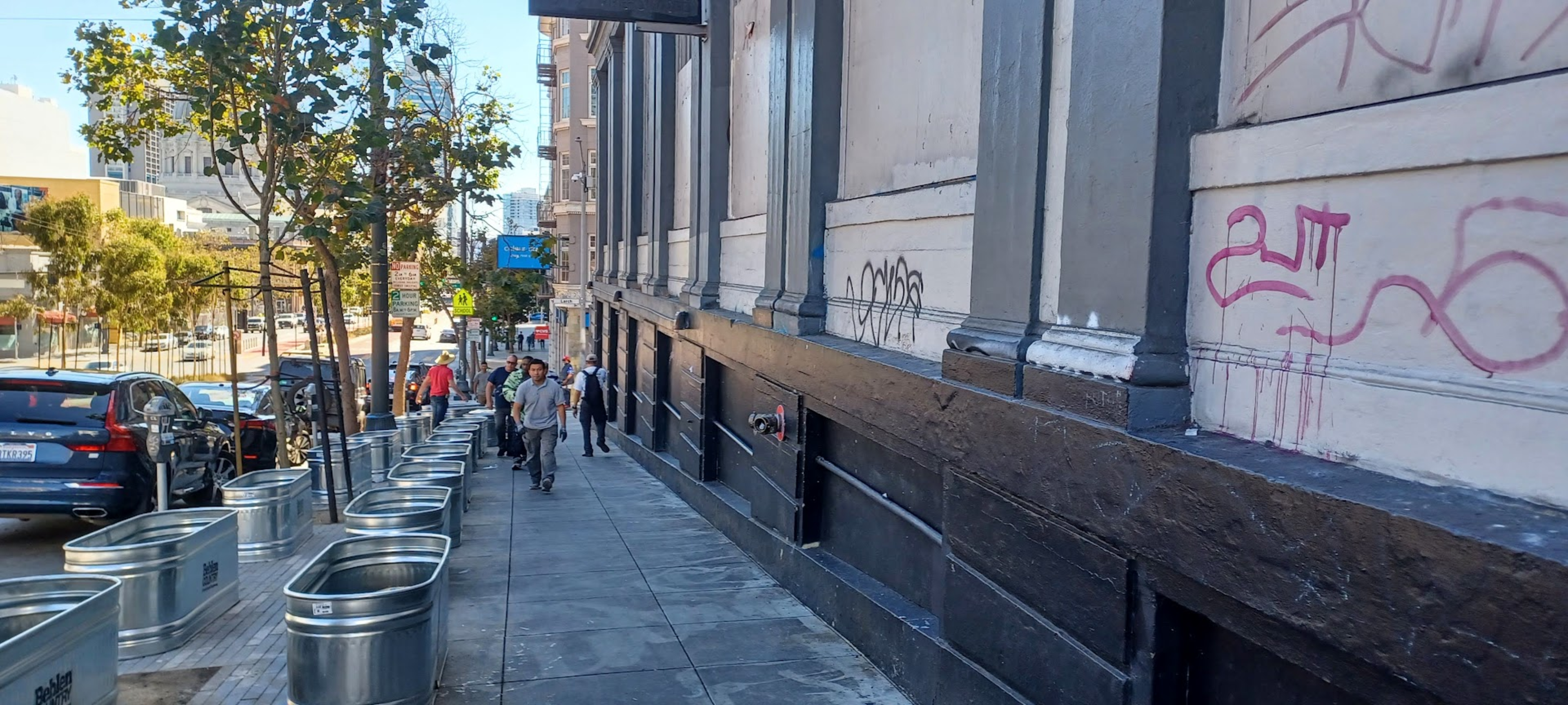 Steel planters line the sidewalks as pedestrians pass by.