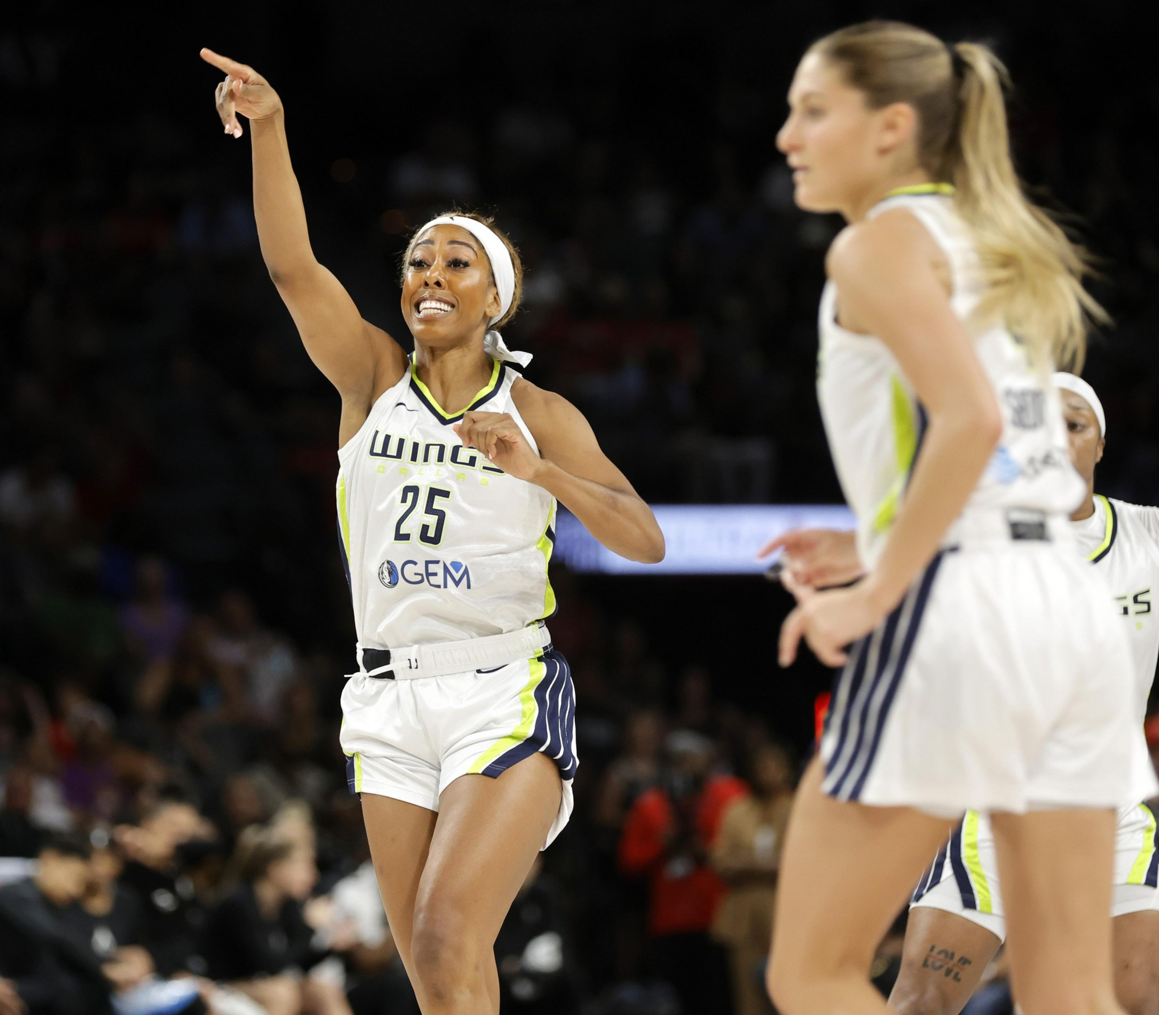 A basketball player in a white uniform with the number 25 points energetically during a game. Another player in the foreground is partially visible.