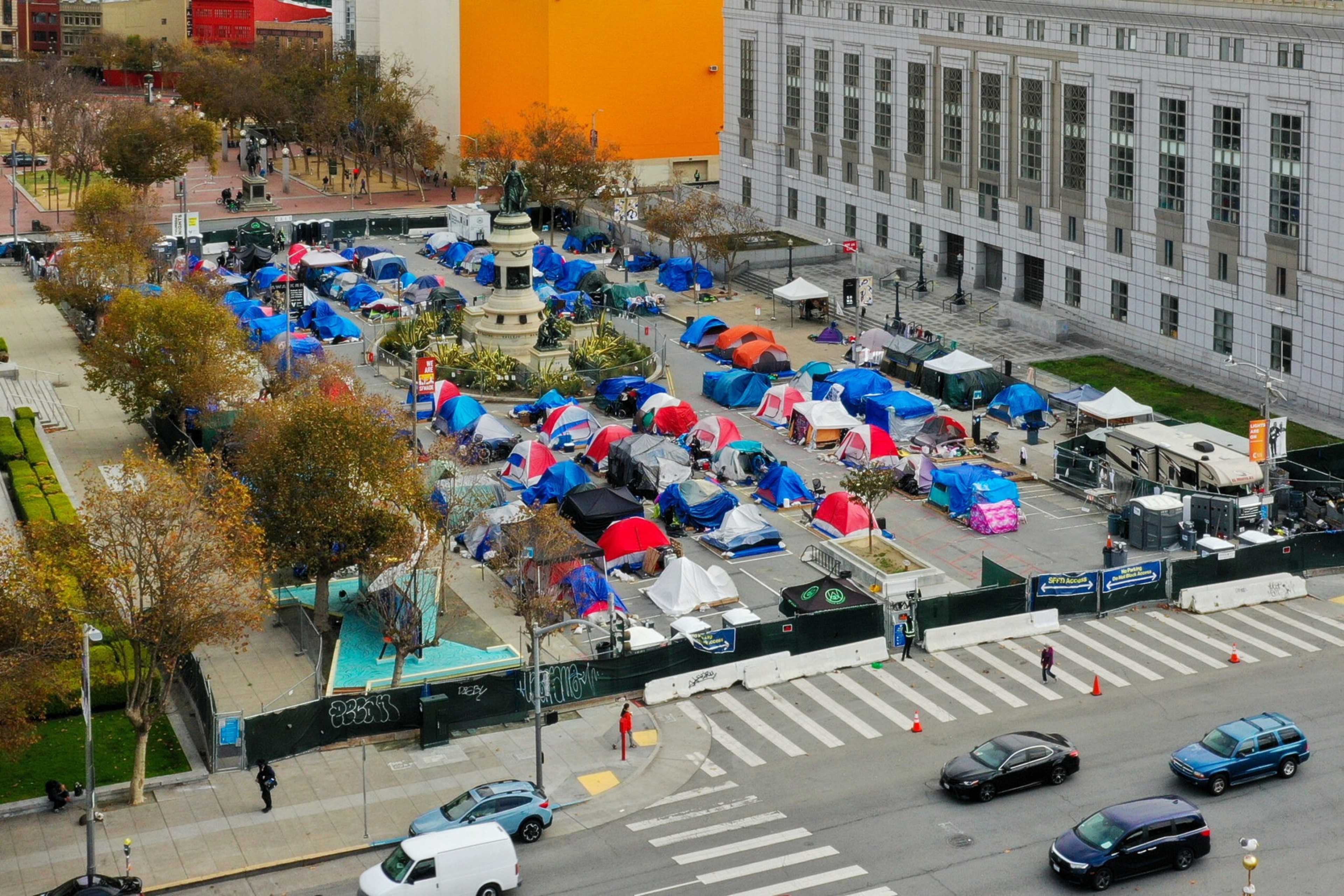 A city block crowded with many colorful tents forms a large encampment around a monument, bordered by a sidewalk and streets with cars.