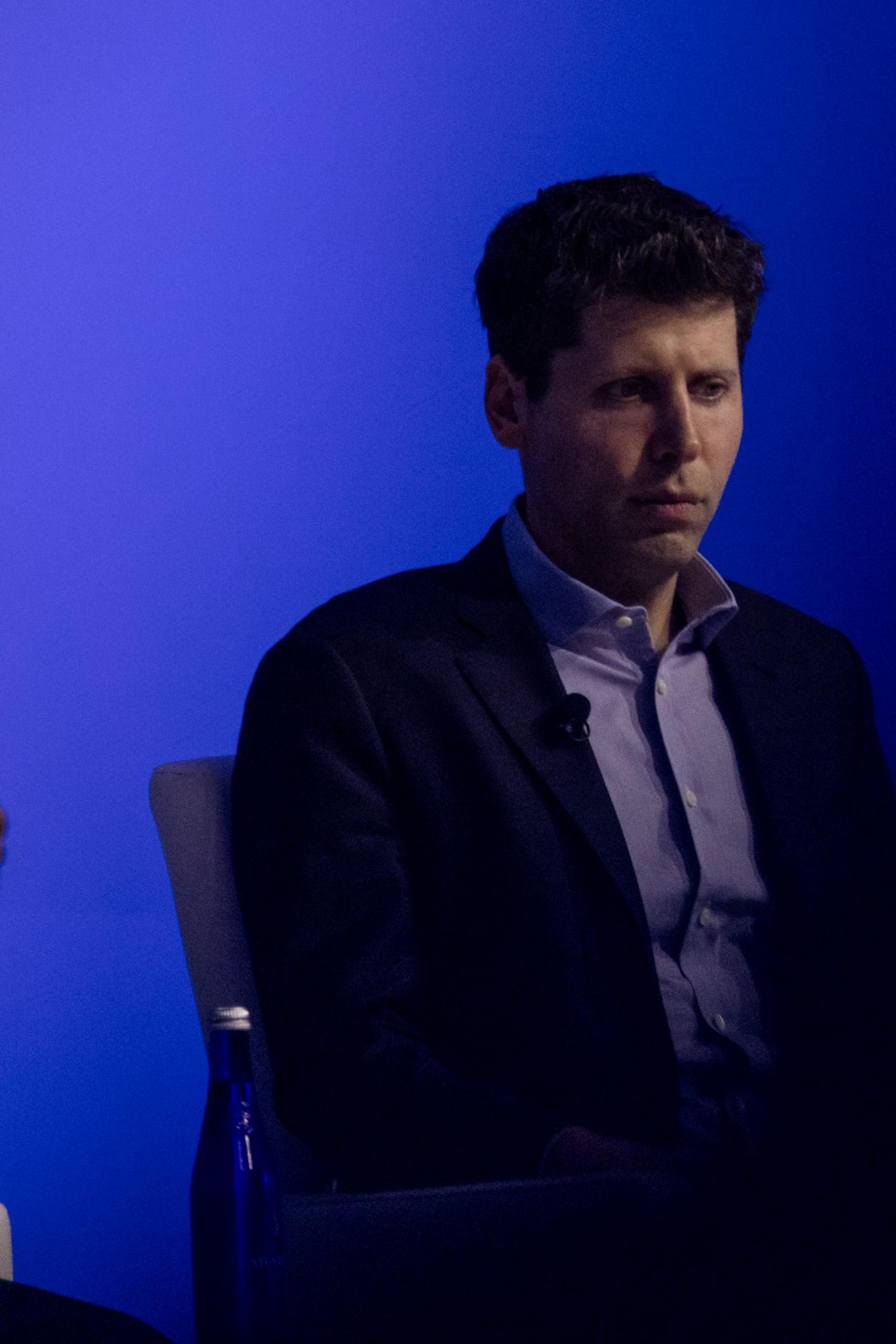 Sam Altman, CEO of OpenAI, looks offscreen with a blue background.