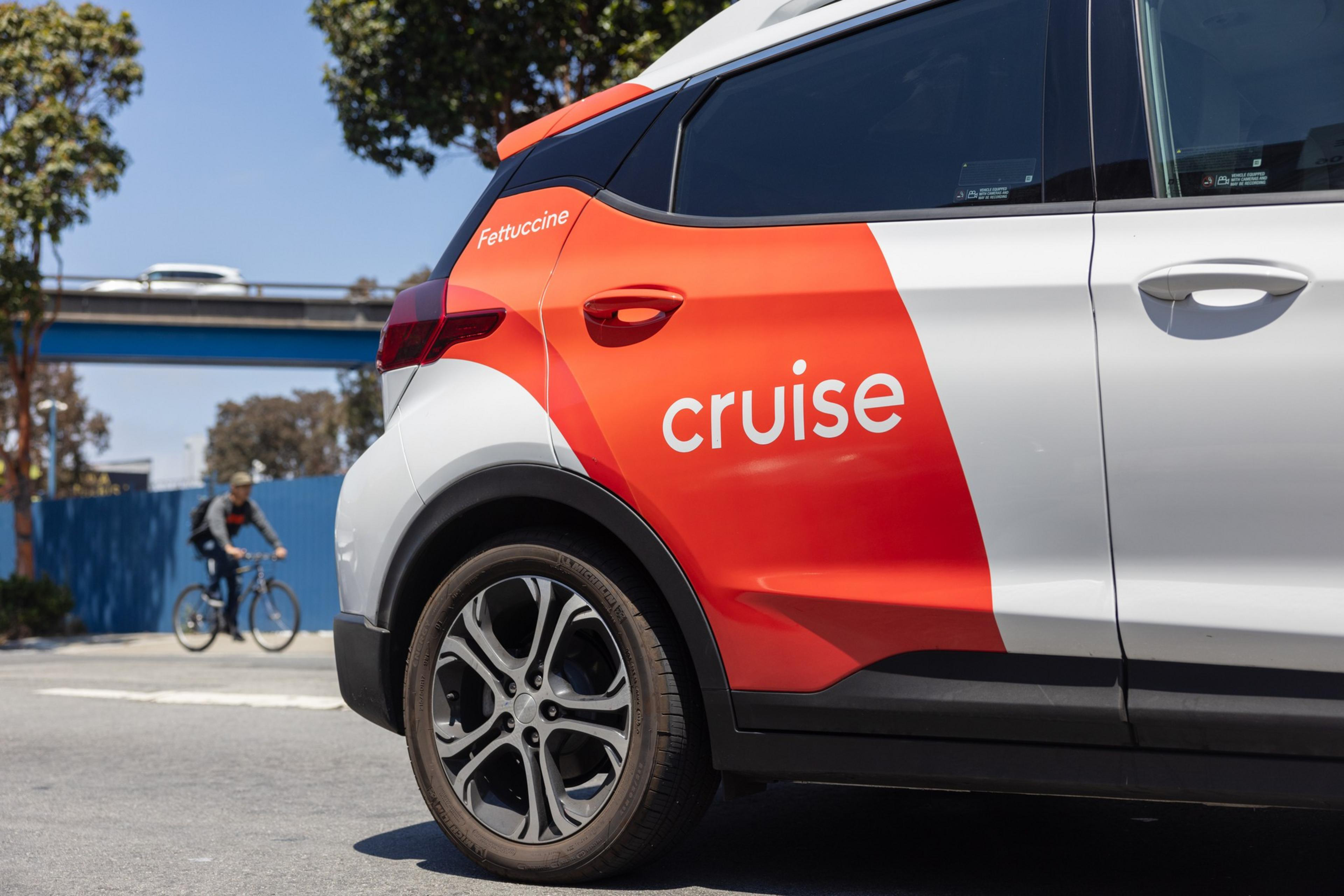 The rear passenger side of a white painted coupe vehicle has a wide orange ribbon with the word Cruise in white within it.