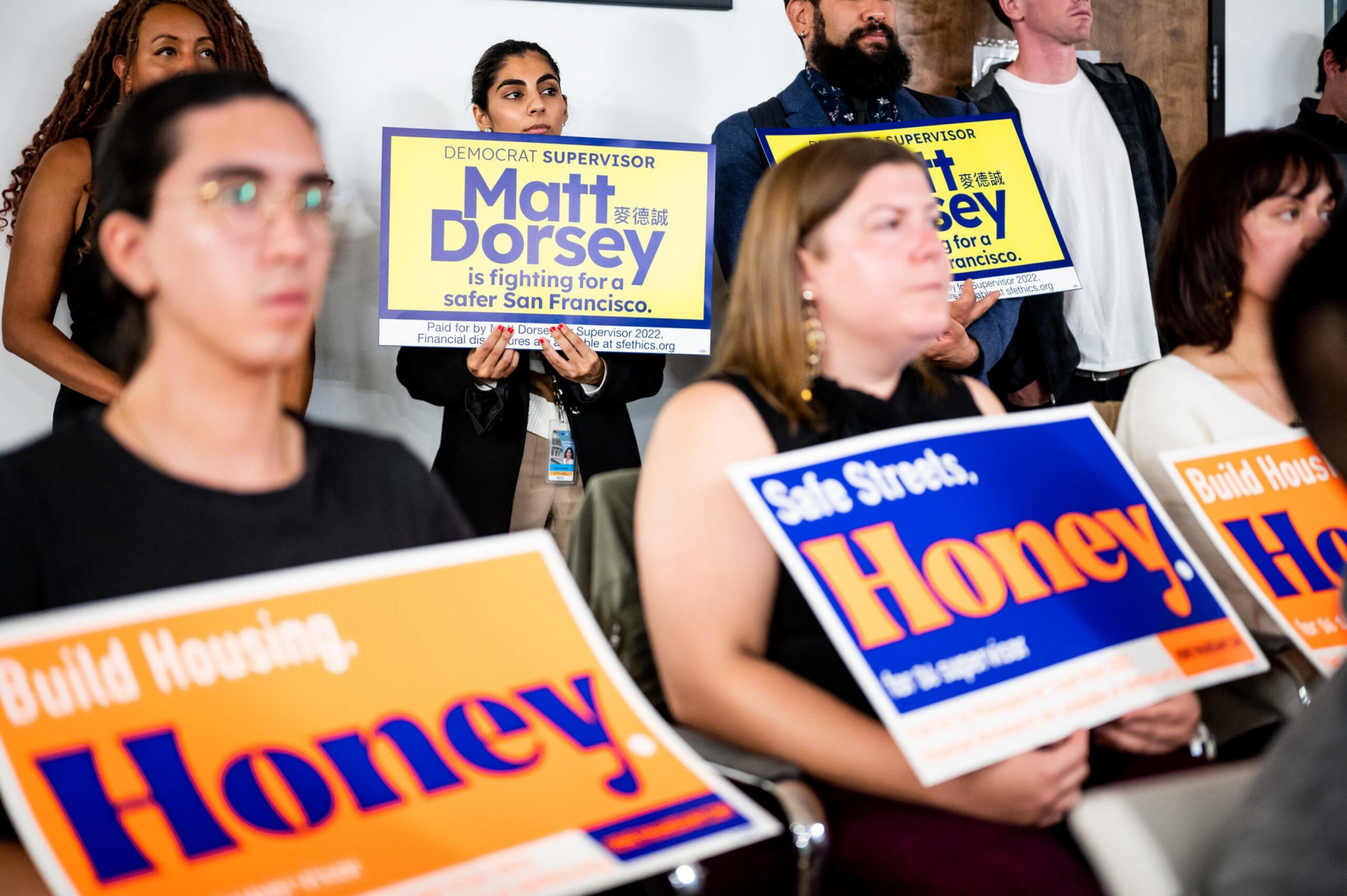 Several people are holding campaign signs supporting Matt Dorsey for San Francisco supervisor and Honey Mahogany for safer streets and housing.