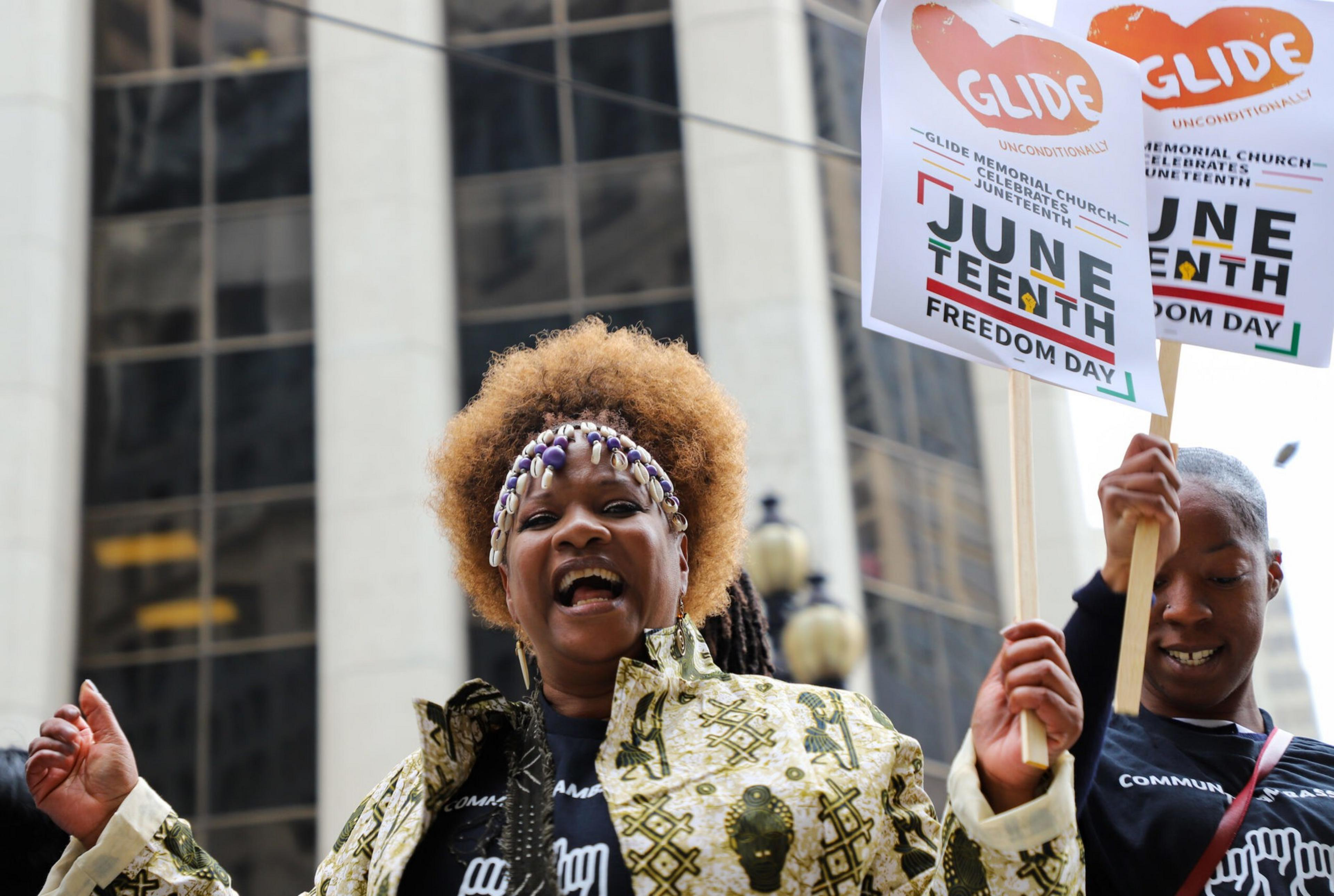 Two people celebrate Juneteenth, holding signs that read &quot;Freedom Day.&quot;