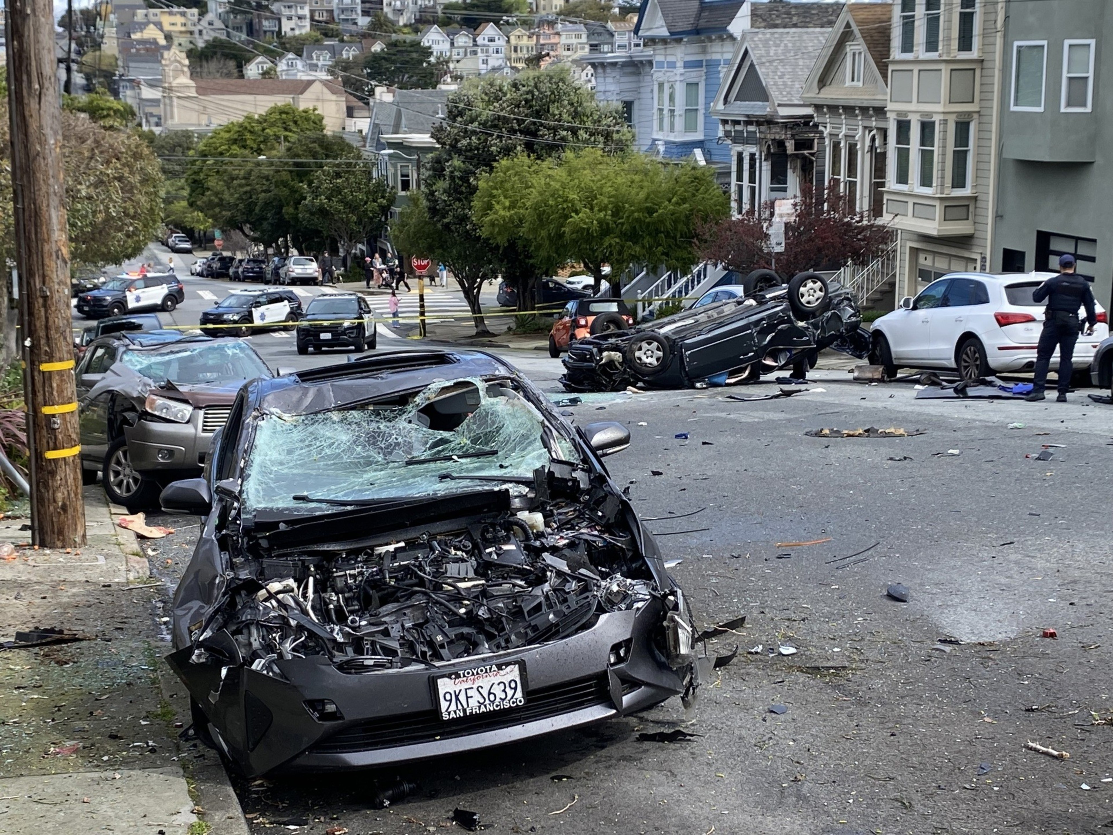 An overturned car and a severely damaged car on a city street with debris around.