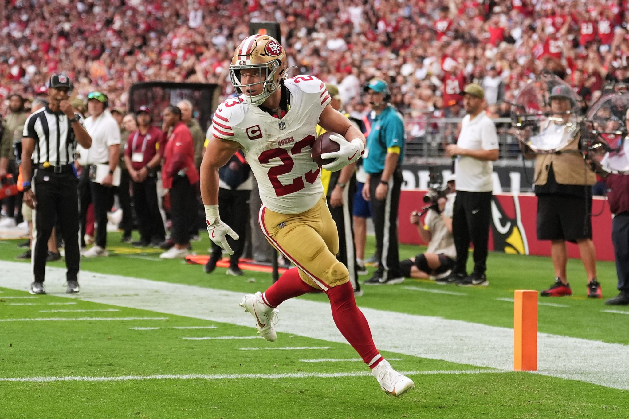 A football player wearing a San Francisco 49ers uniform runs near the end zone with the ball in hand during a game.