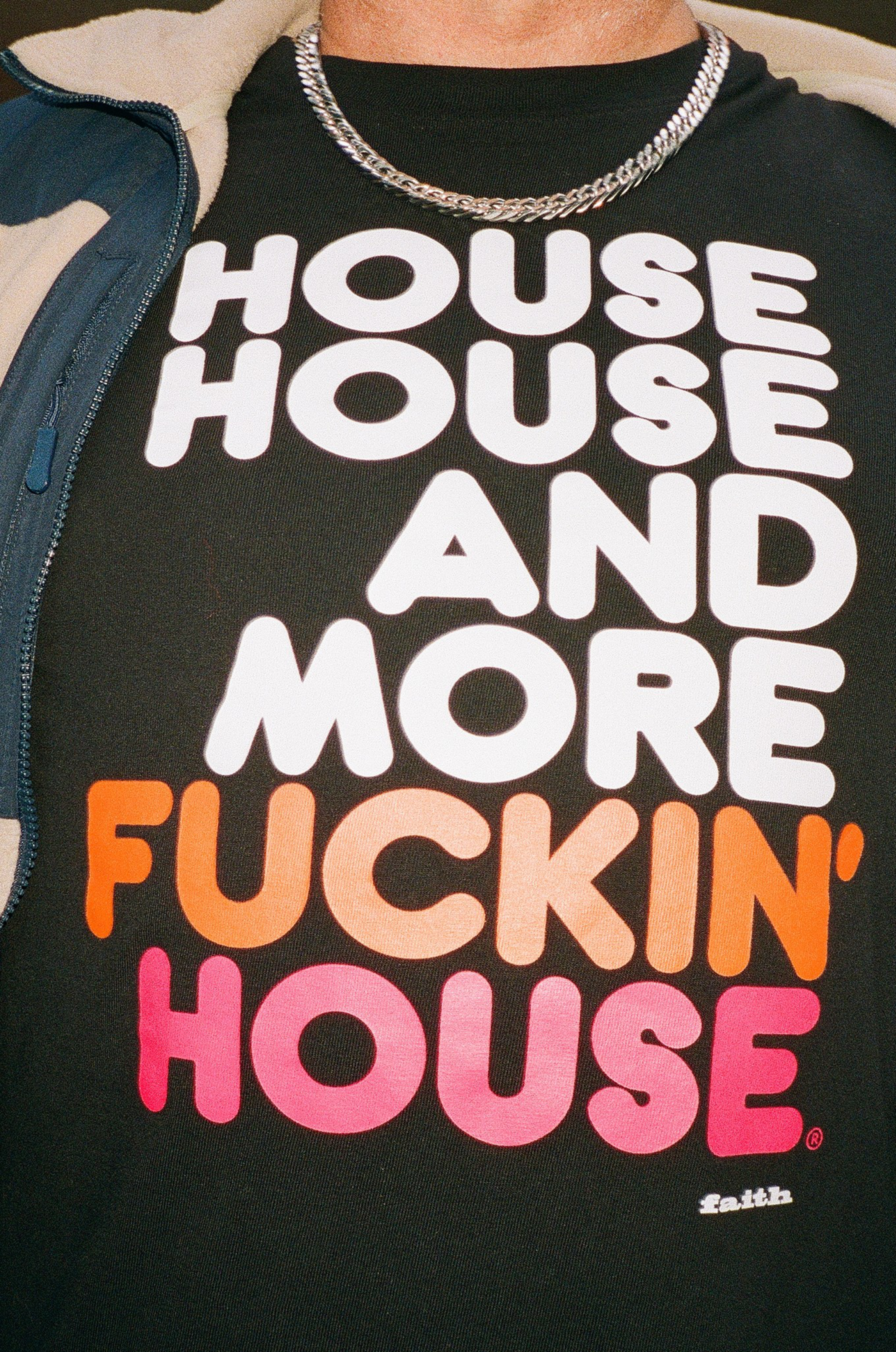 A black shirt with large bold text saying "HOUSE HOUSE AND MORE FUCKIN' HOUSE" in white, orange, and pink, worn with a silver chain necklace.