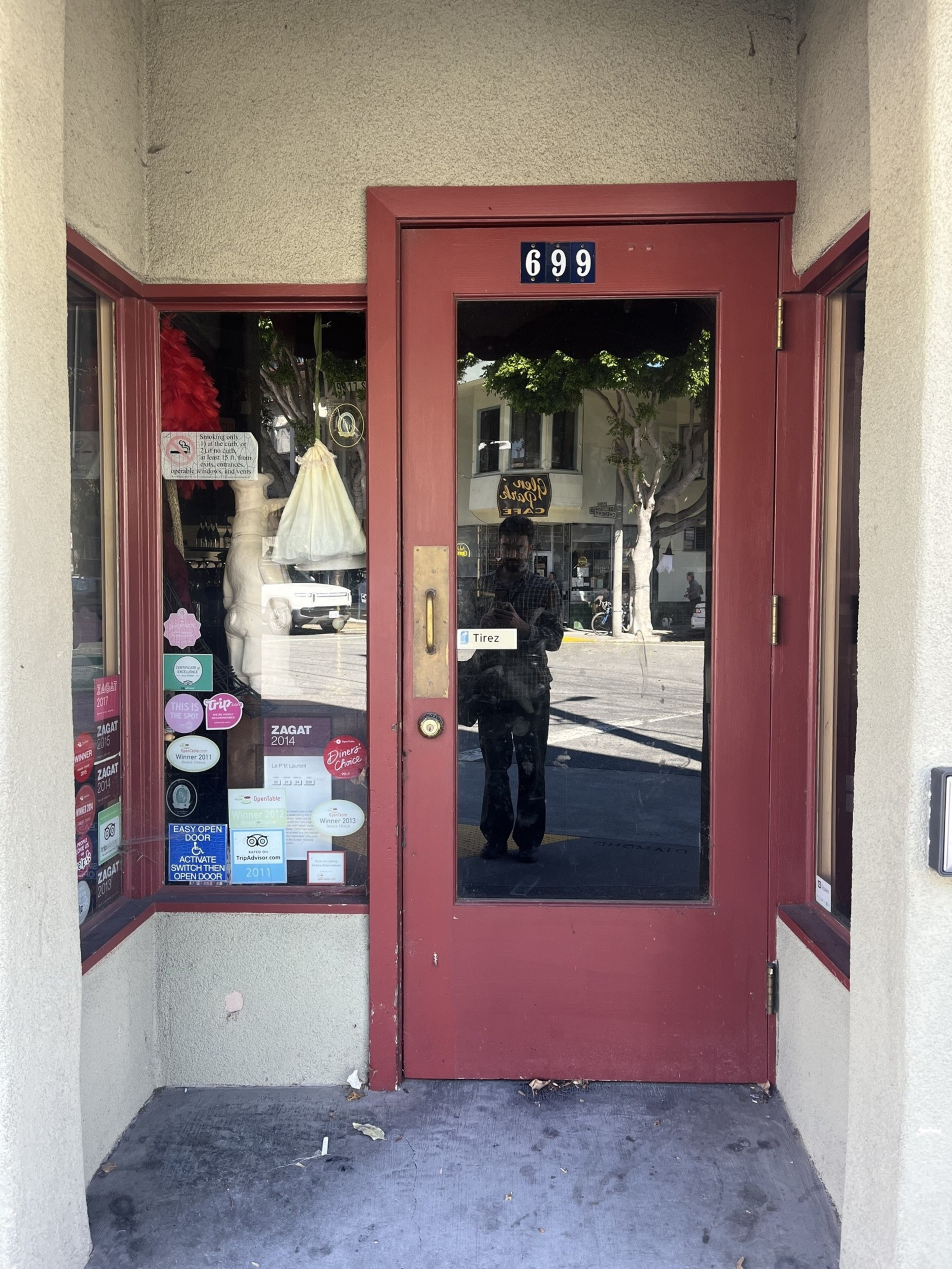 A red-framed glass door labeled 699 with multiple stickers on the left window, a “Tirez” pull sign, and a reflection of a person taking the photo.