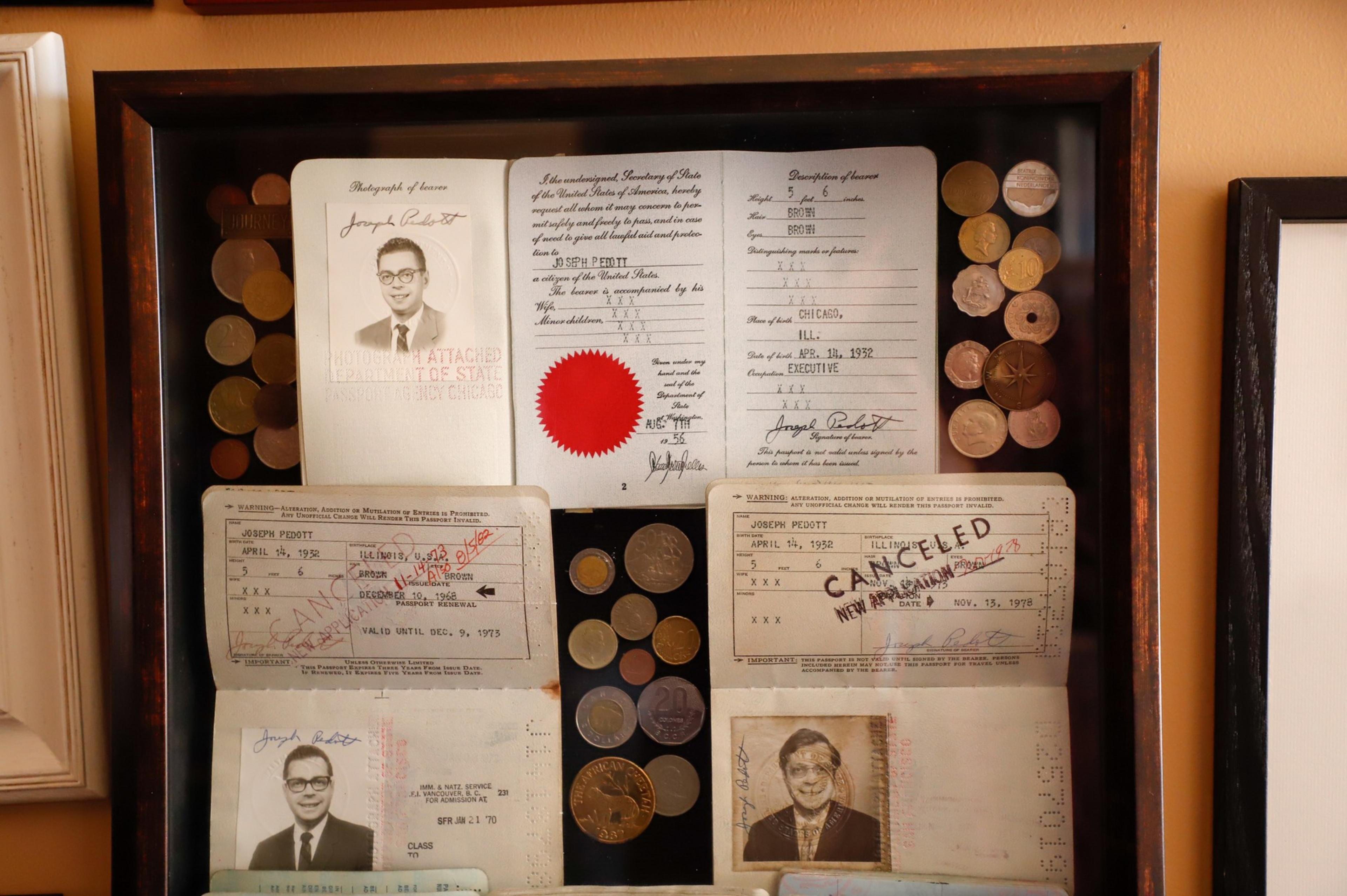 A framed collection of vintage documents and photos with official stamps, signatures, and various coins arranged around them.