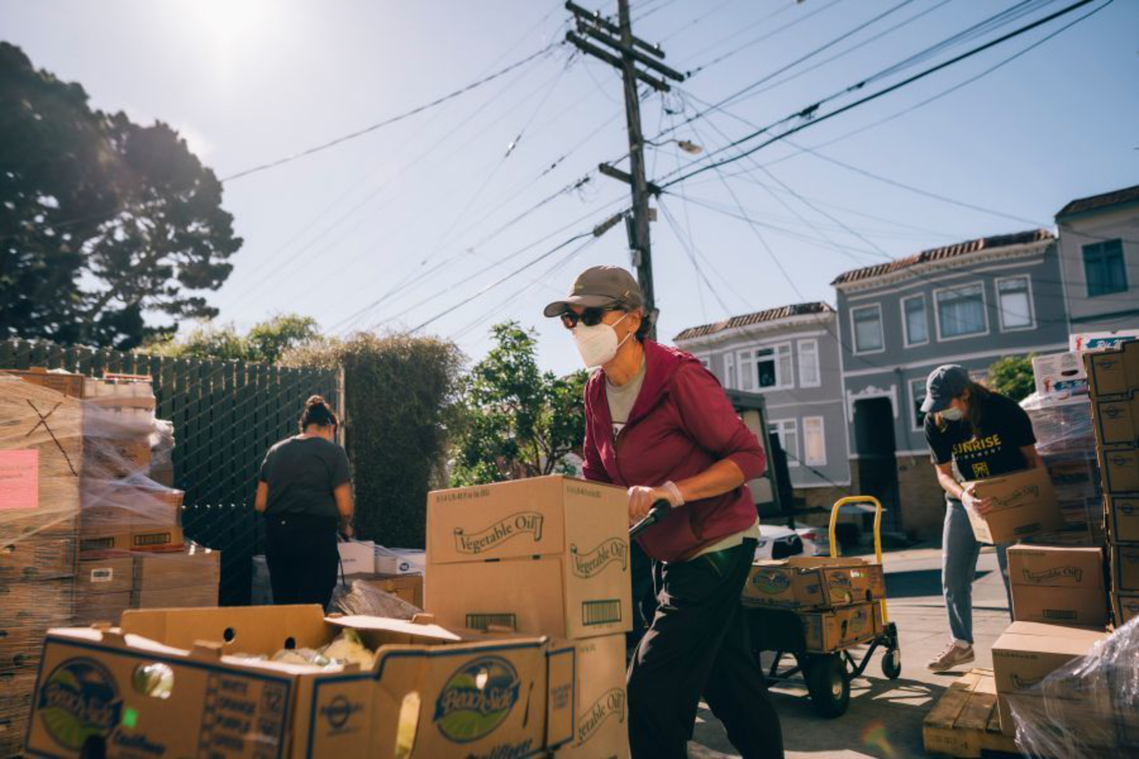 People are distributing supplies from pallets on a sunny street.