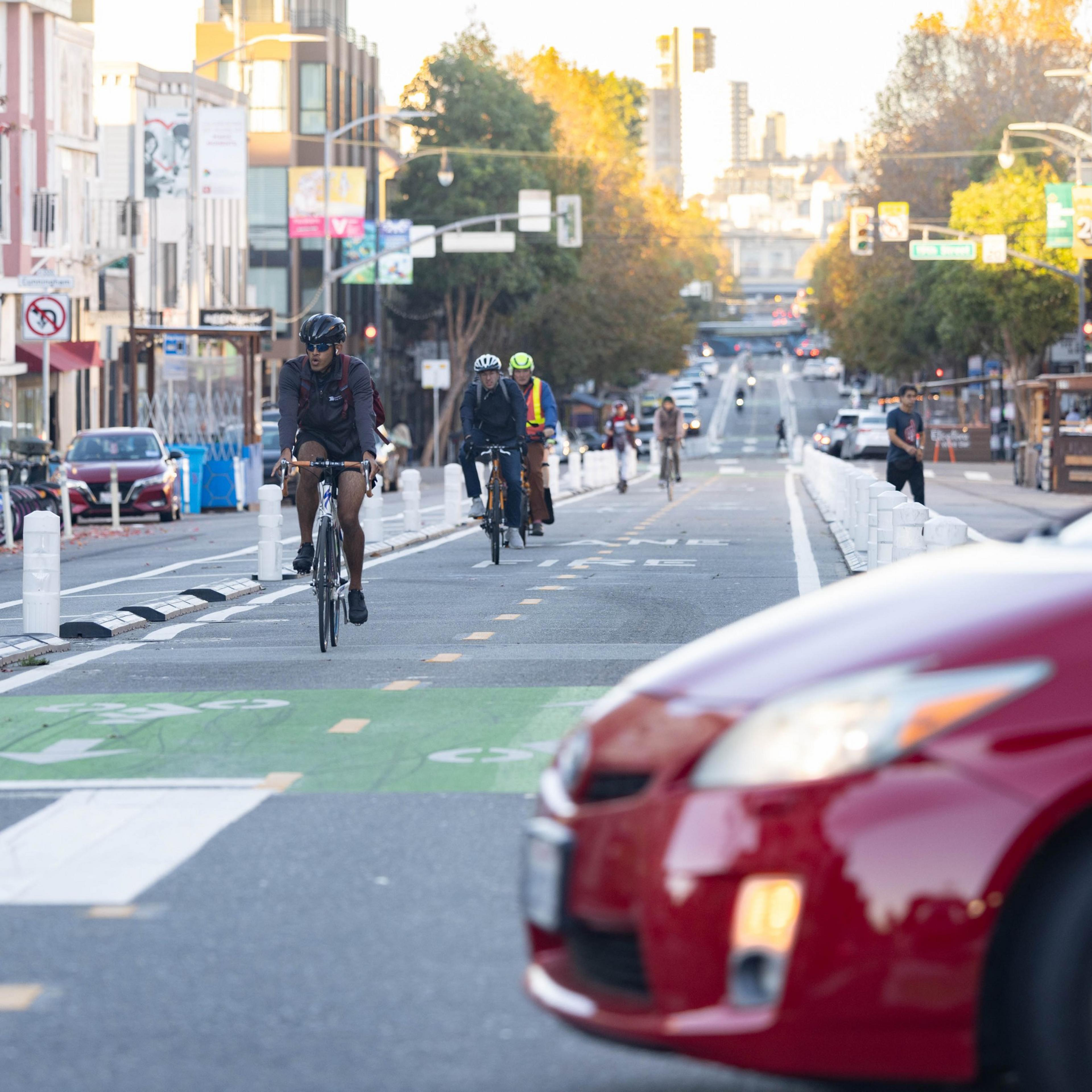A long view down a street with a green-painted cycle track, and a red car nosing into the intersection.