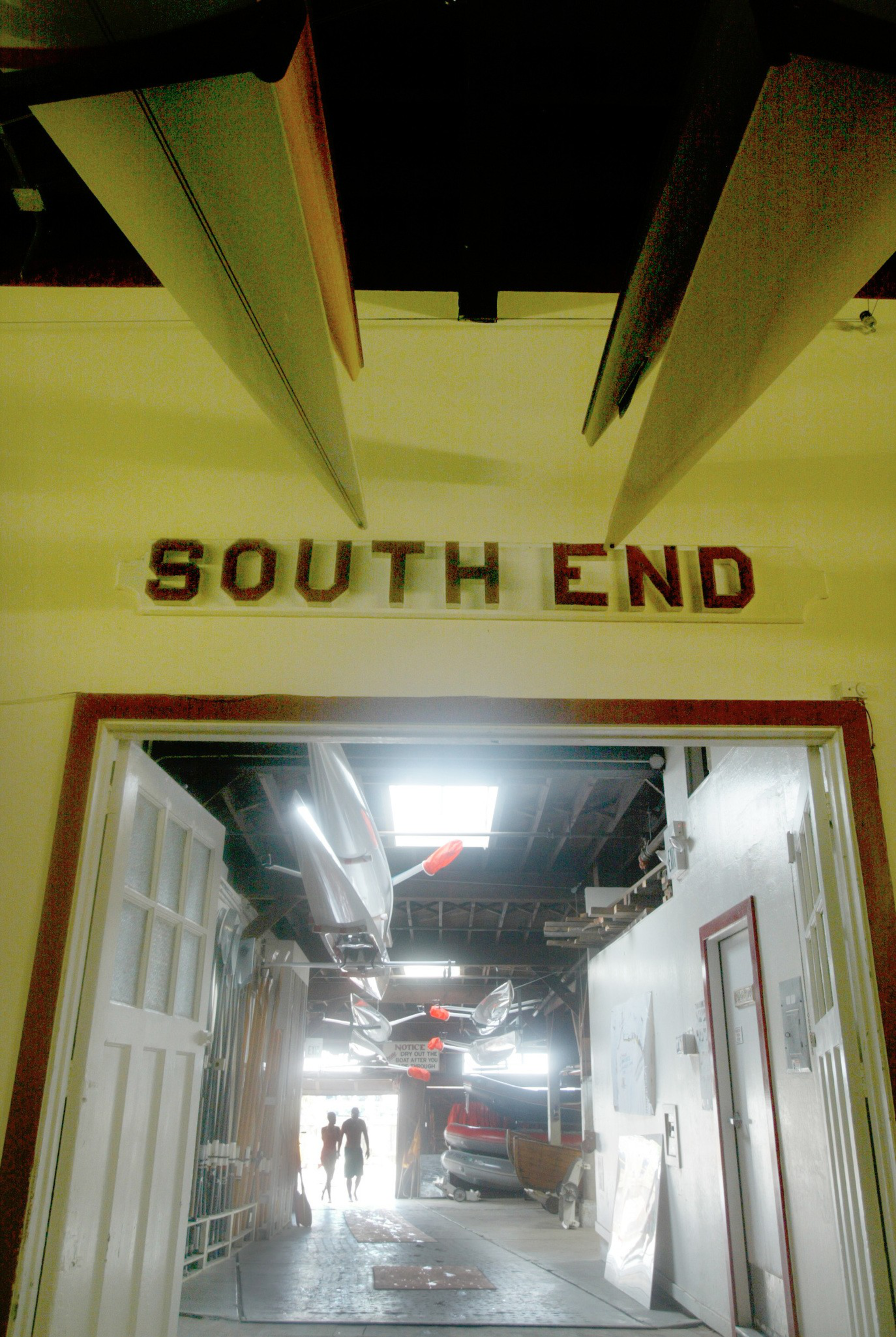 A doorway labeled “SOUTH END” leads into a boathouse with kayaks and canoes hanging from the ceiling and two people walking toward the light at the far end.