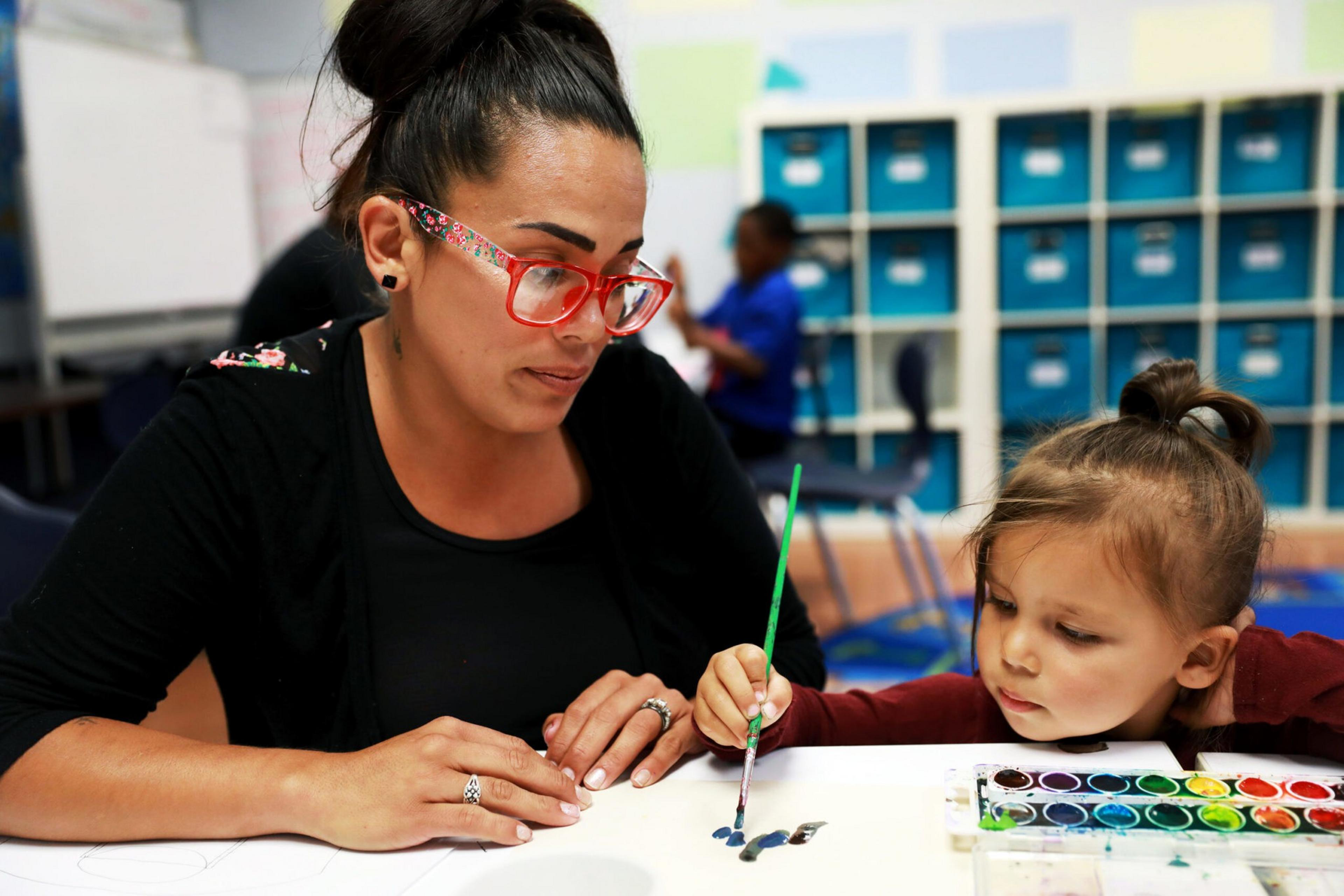 A person and a child at a desk in a classroom.