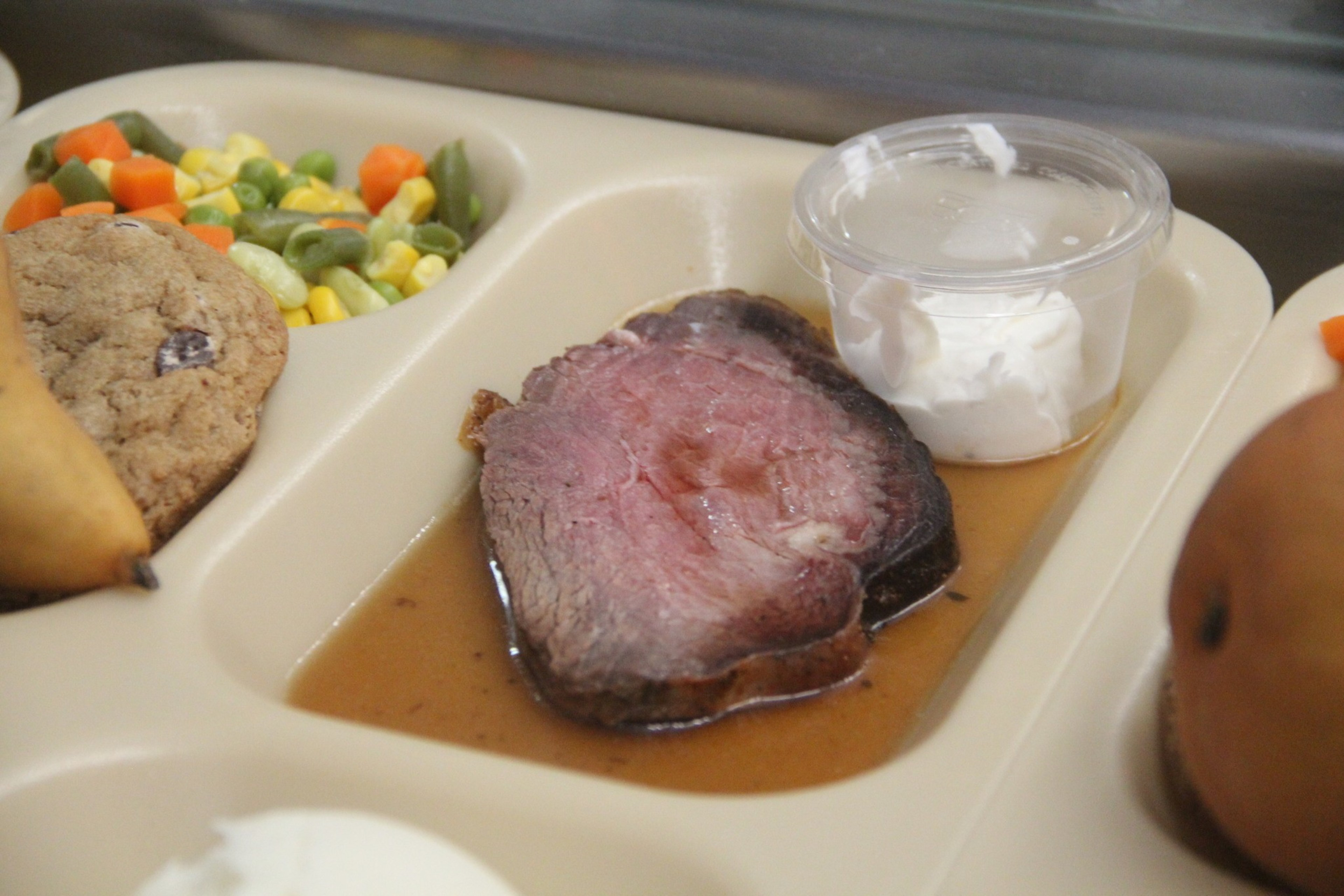 A plate of prime rib, mixed of greens and mashed potatoes, a pear and cookie.