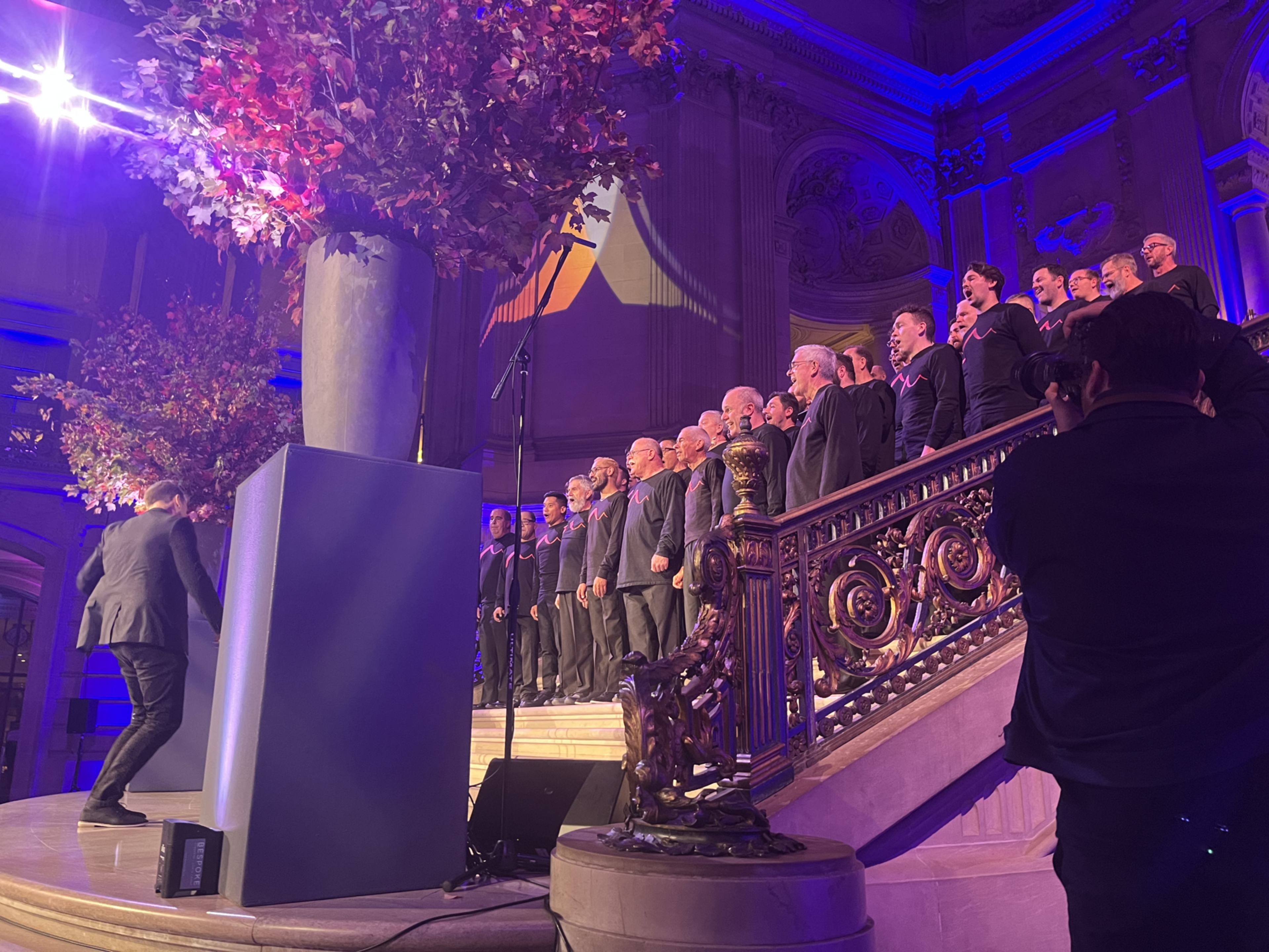 Dozens of men in black T-shirts sing on the steps of a fancy government building inside.