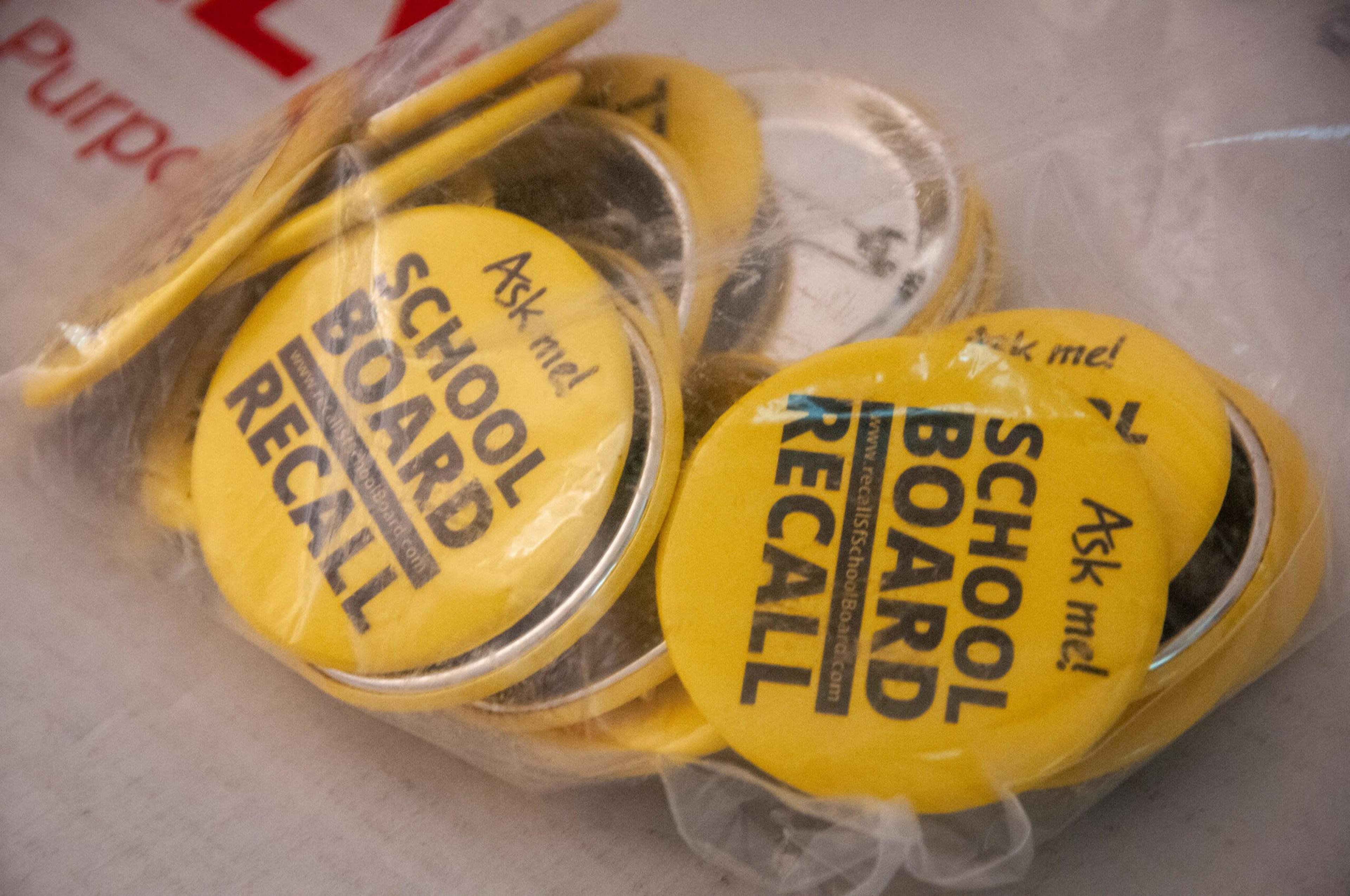 Yellow buttons with black text reading "Ask me! SCHOOL BOARD RECALL" are inside a clear plastic bag.