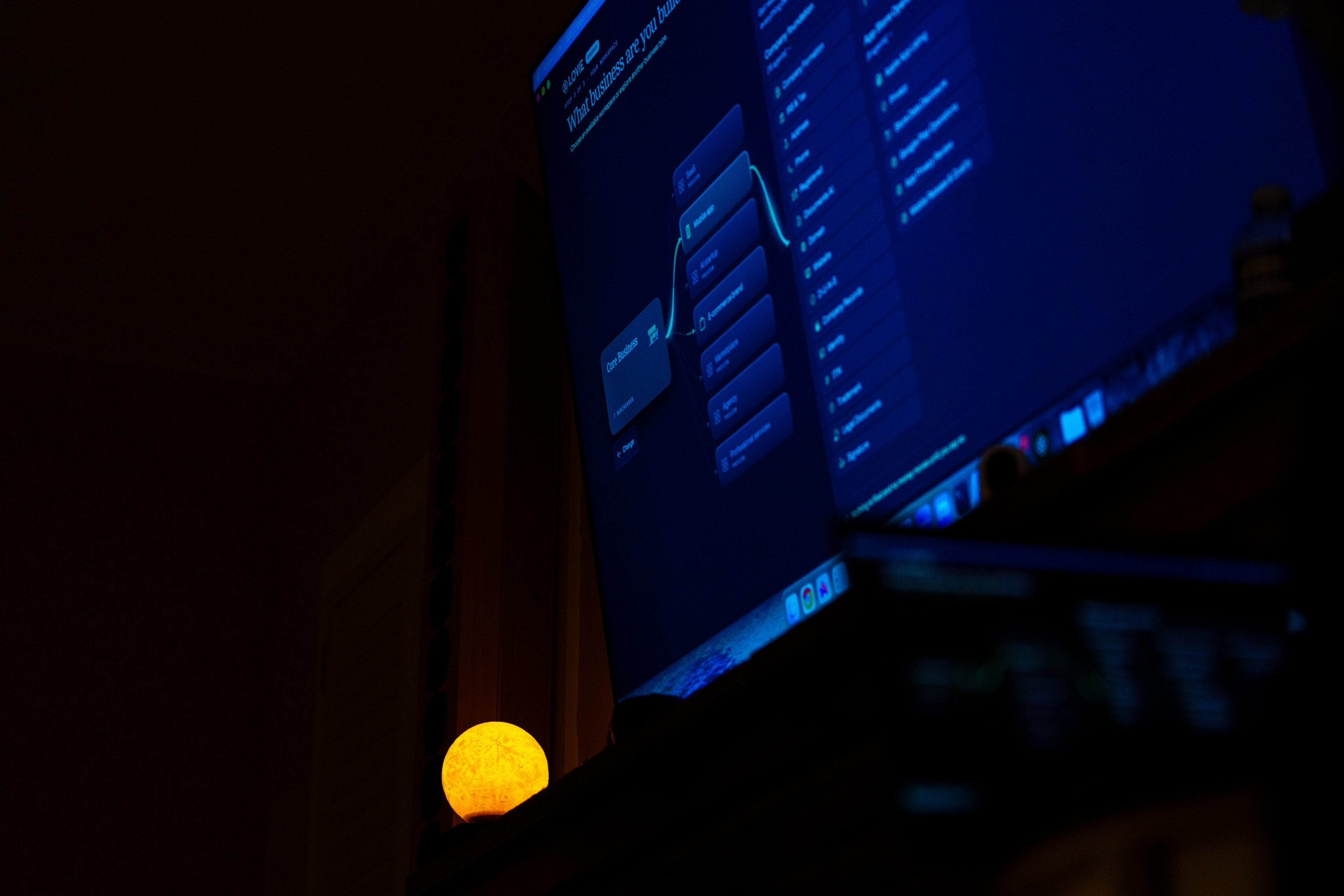 A glowing orange spherical light sits on a shelf below a dark computer ...