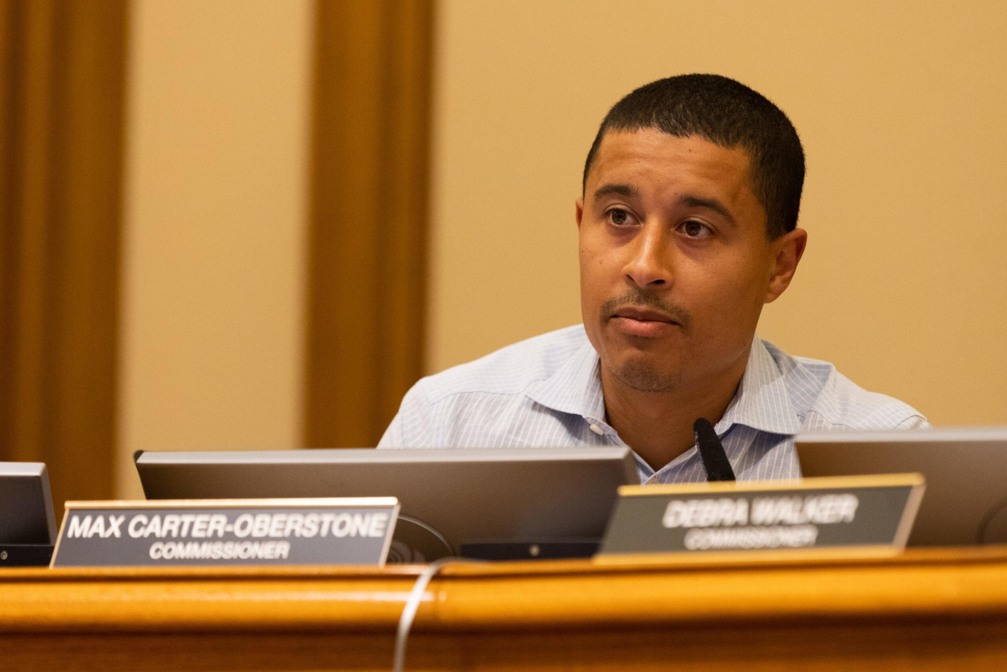 A man sits at a desk with nameplates, focused intently during a meeting.