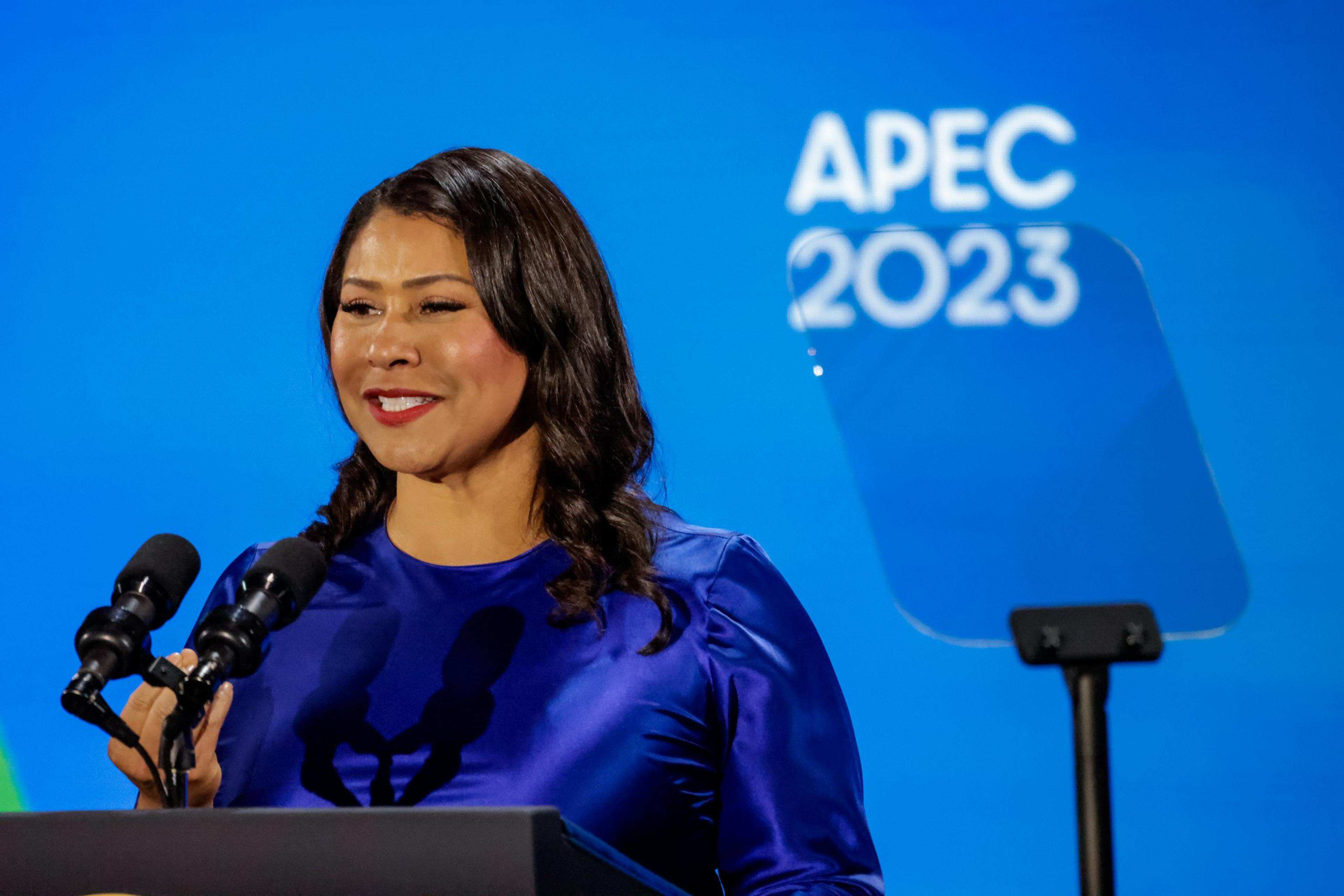 A woman in a purple dress stands before a microphone. 