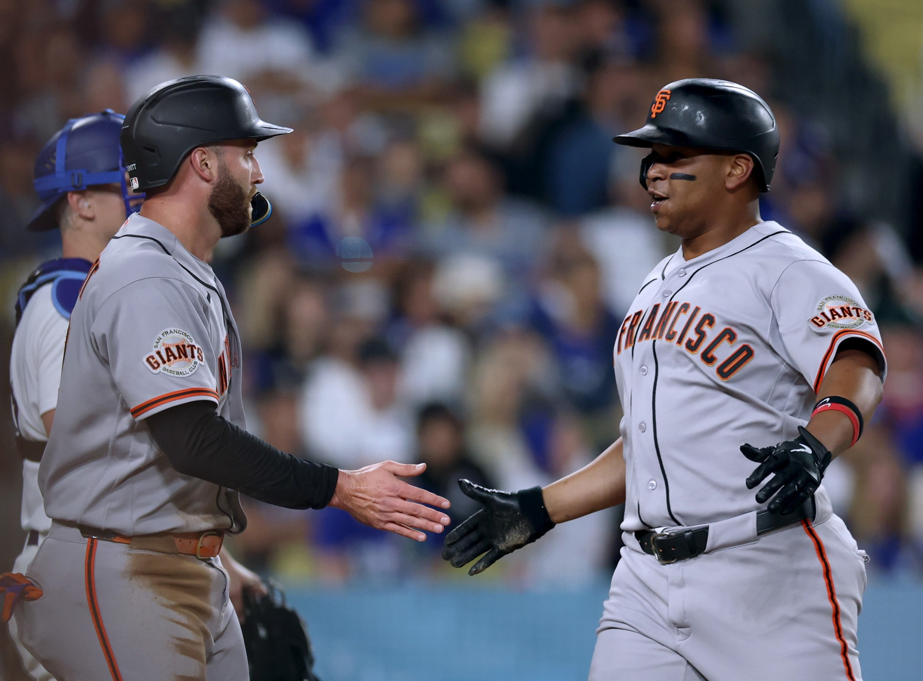 Two San Francisco Giants baseball players wearing gray uniforms and black helmets are about to high-five during a game.