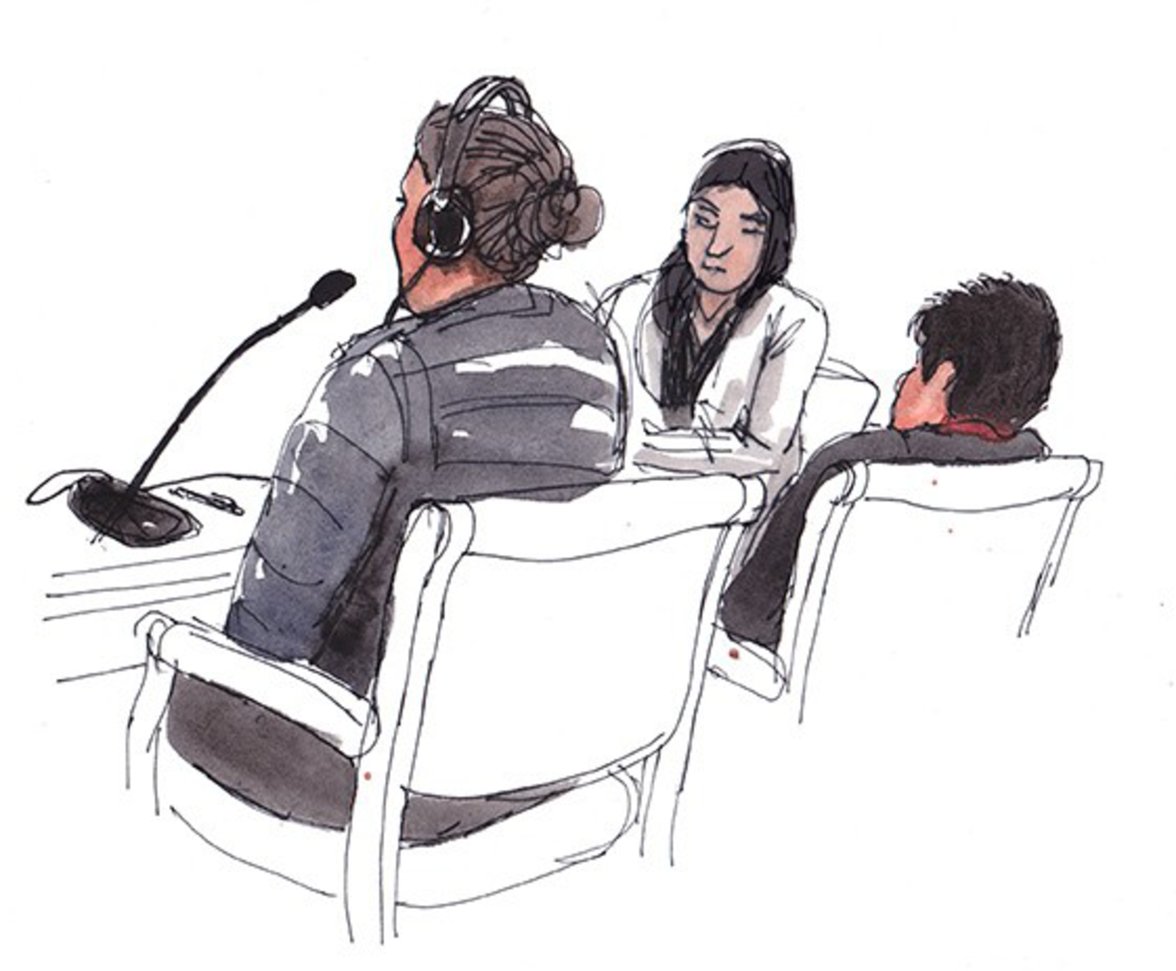 Three people sit in chairs facing forward; one wears headphones and speaks into a microphone, while the other two listen attentively.