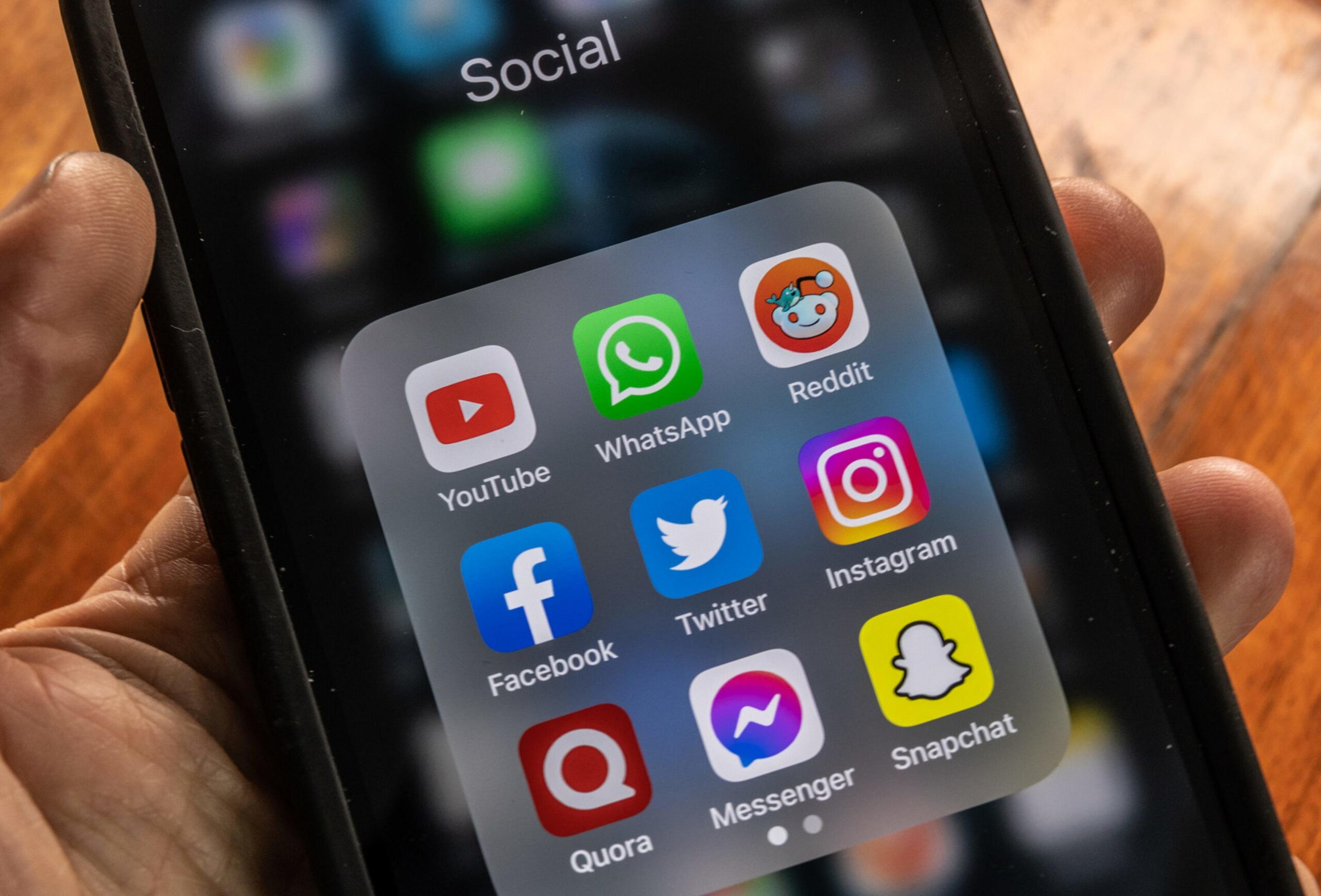 A smartphone screen displays a folder labeled "Social" containing YouTube, WhatsApp, Reddit, Facebook, Twitter, Instagram, Quora, Messenger, and Snapchat apps.