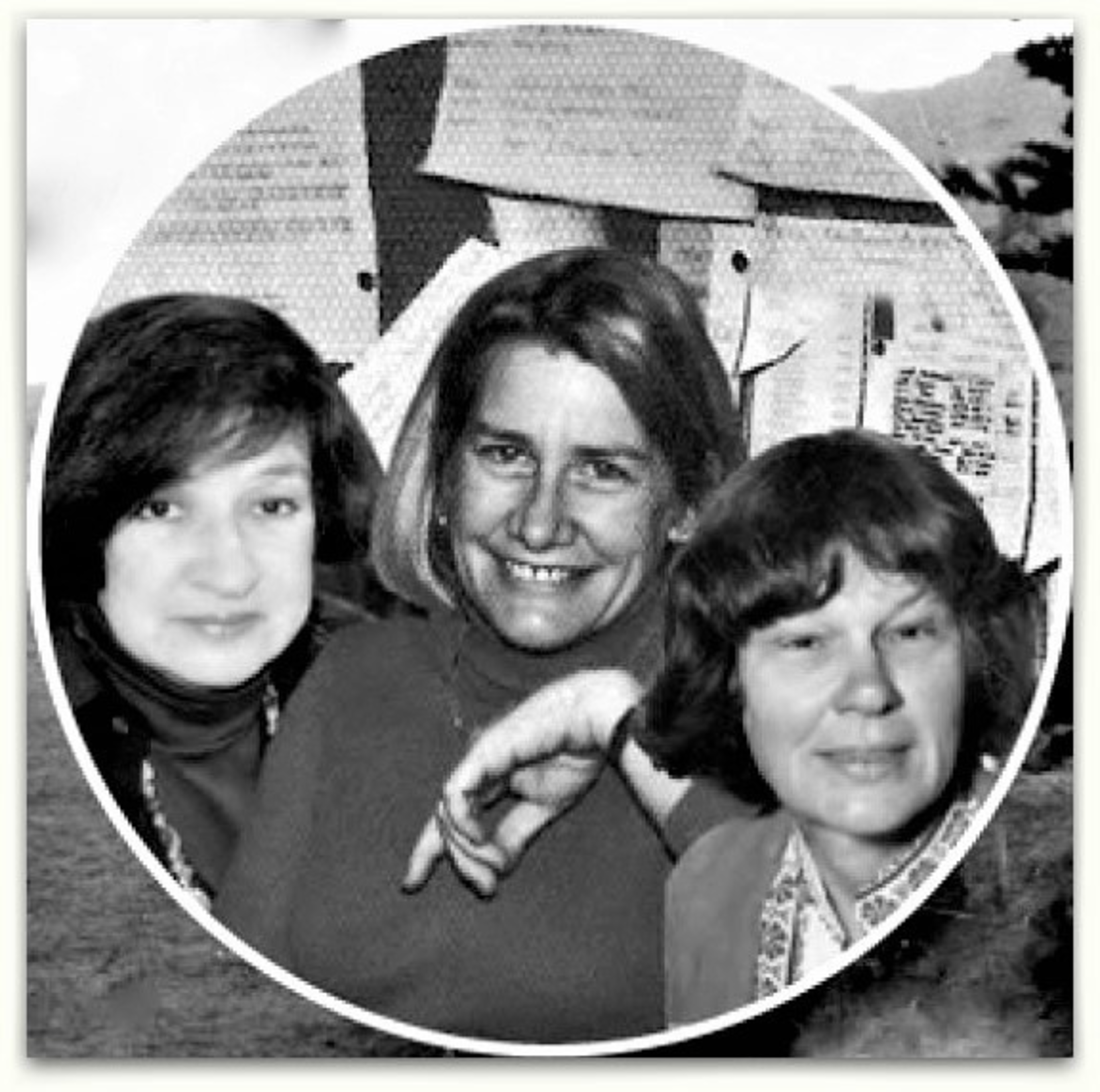 Three women are closely posed, smiling softly; the background shows papers pinned to a wall and an outdoor scene.