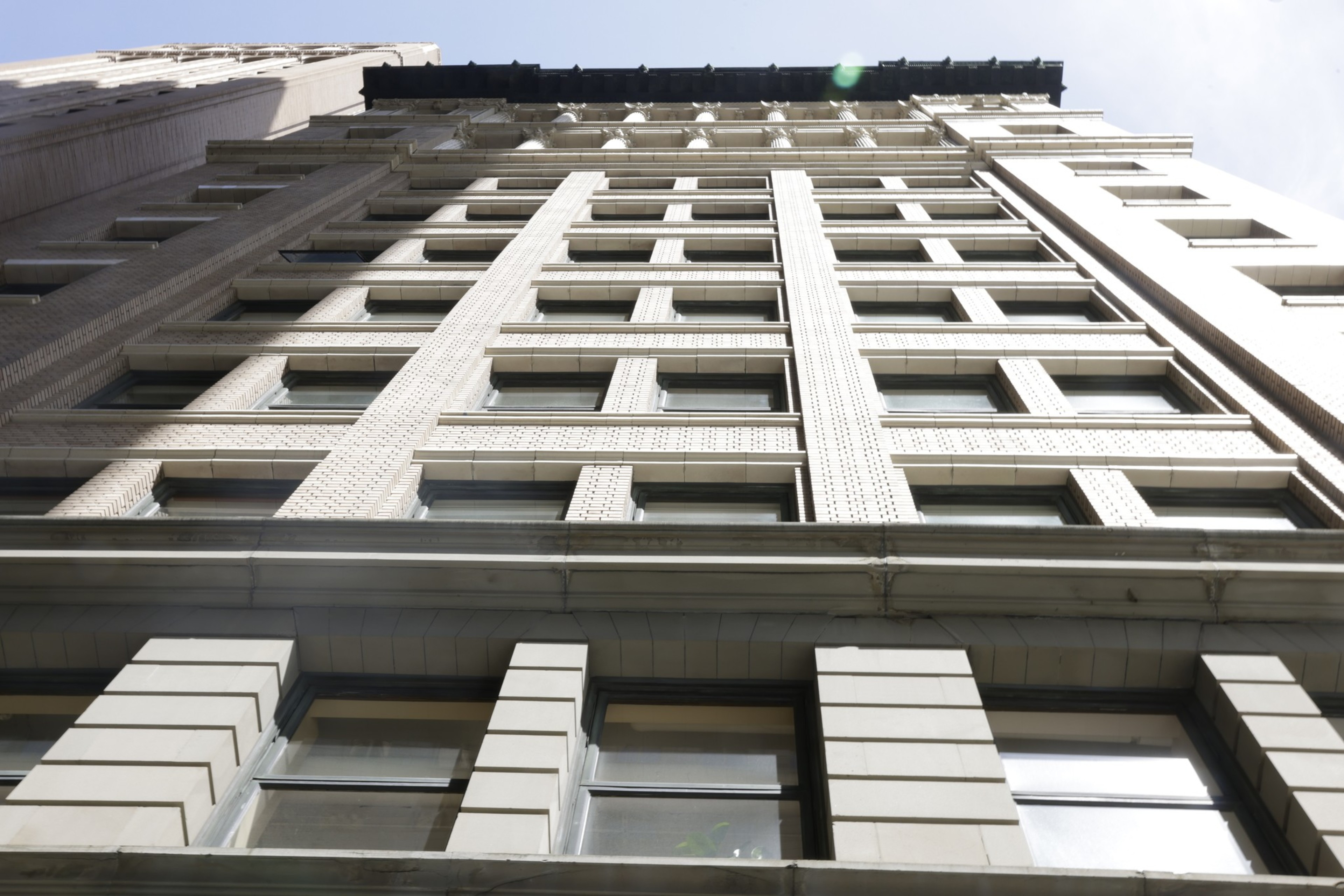 Low-angle view of a tall building's beige facade with repetitive windows under a clear sky.
