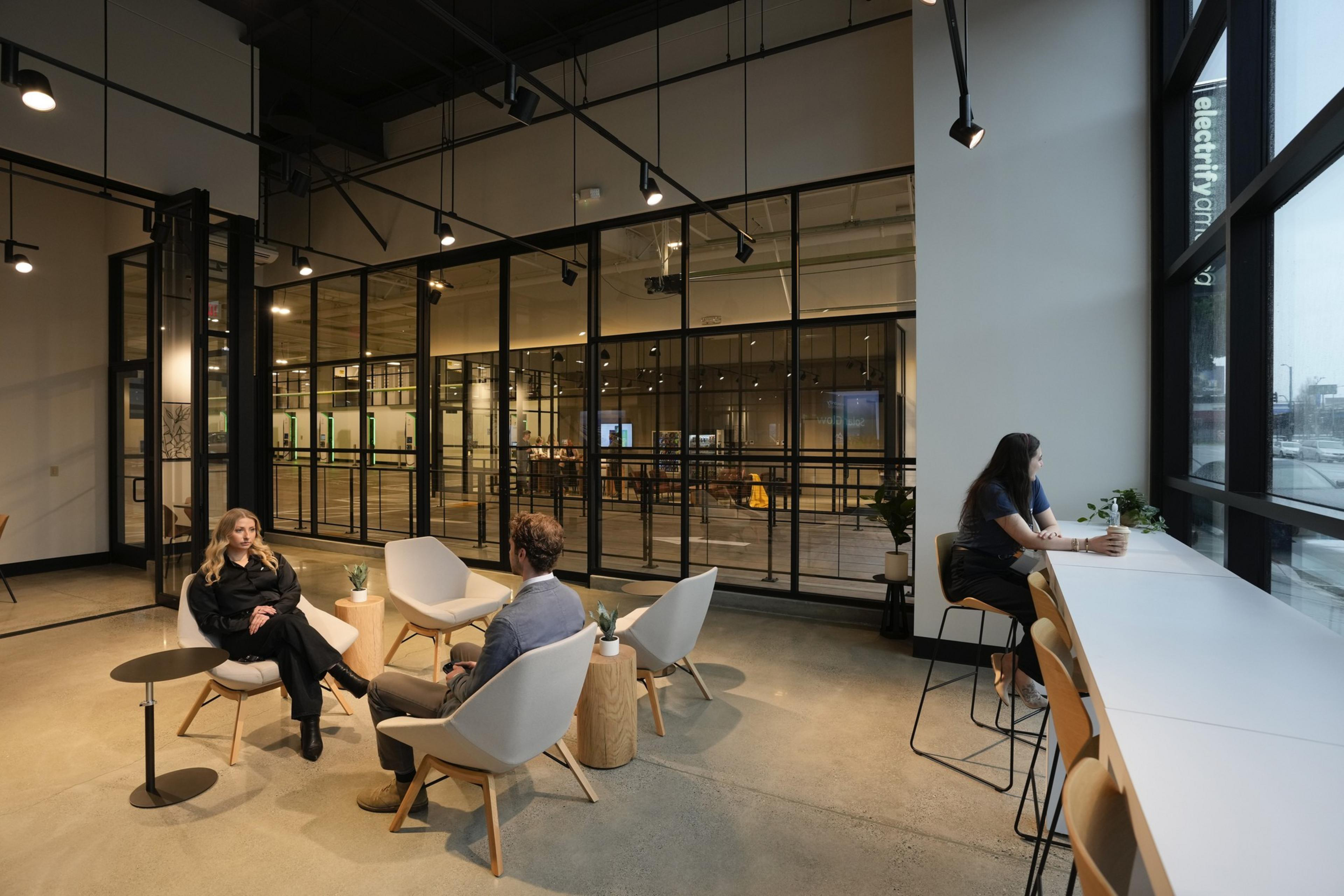 People sit in a lounge with electric vehicles charging nearby.