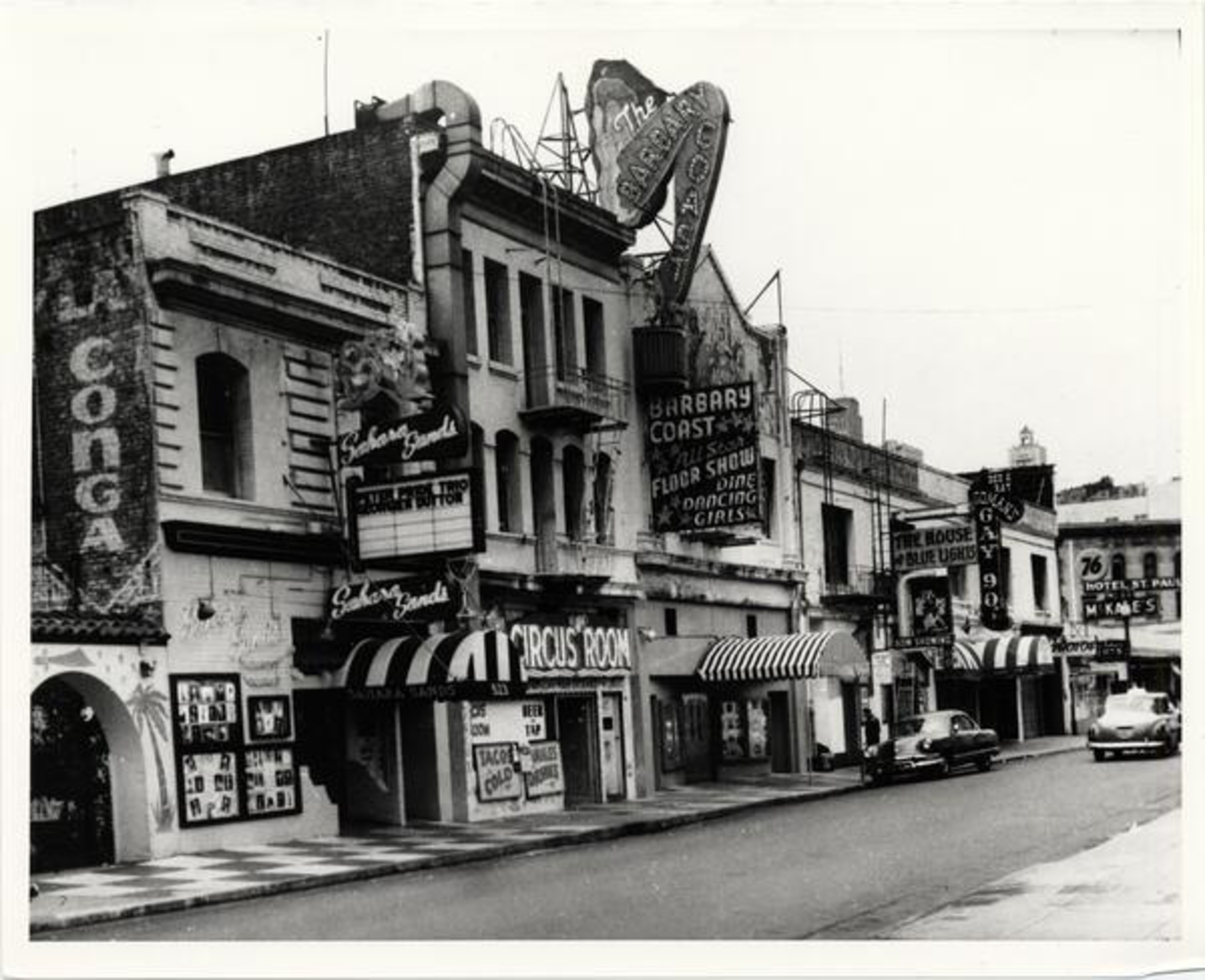 The image shows a vintage city street with old buildings, neon signs, and classic cars. The signs advertise various entertainment venues like nightclubs and theaters.